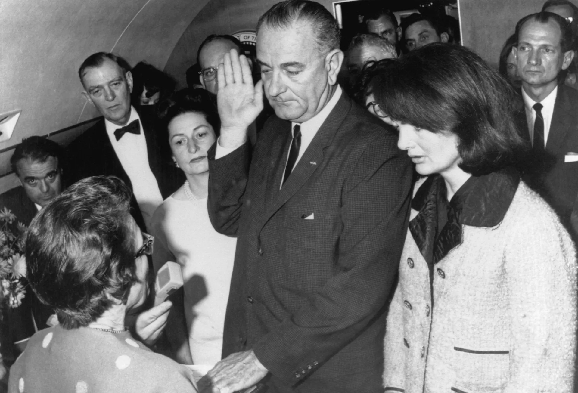 Lyndon B. Johnson fazendo o juramento de posse a bordo do Força Aérea Um, ao lado de uma Jacqueline Kennedy de luto.