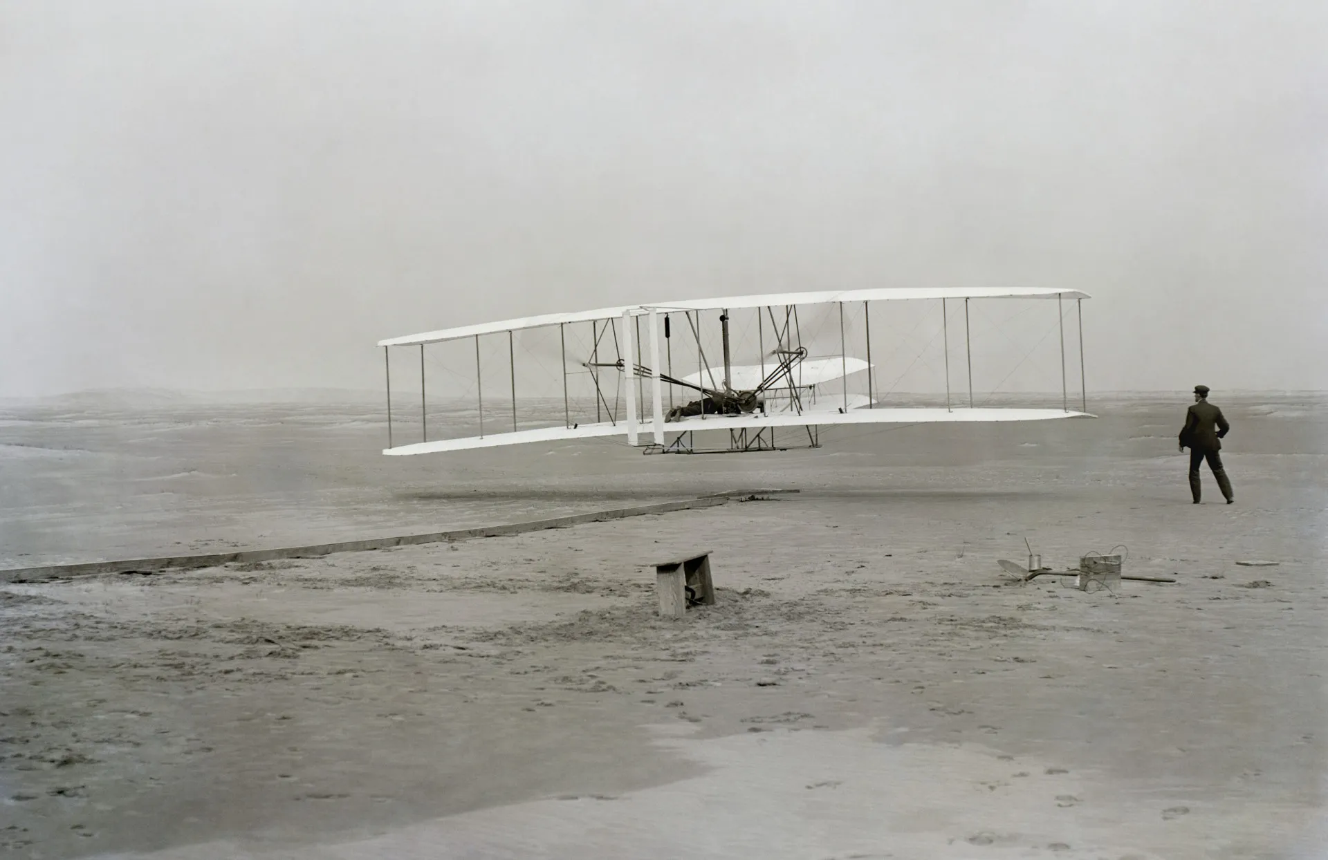 O avião Wright Flyer em seu primeiro voo, com Orville Wright pilotando e Wilber Wright correndo ao lado.