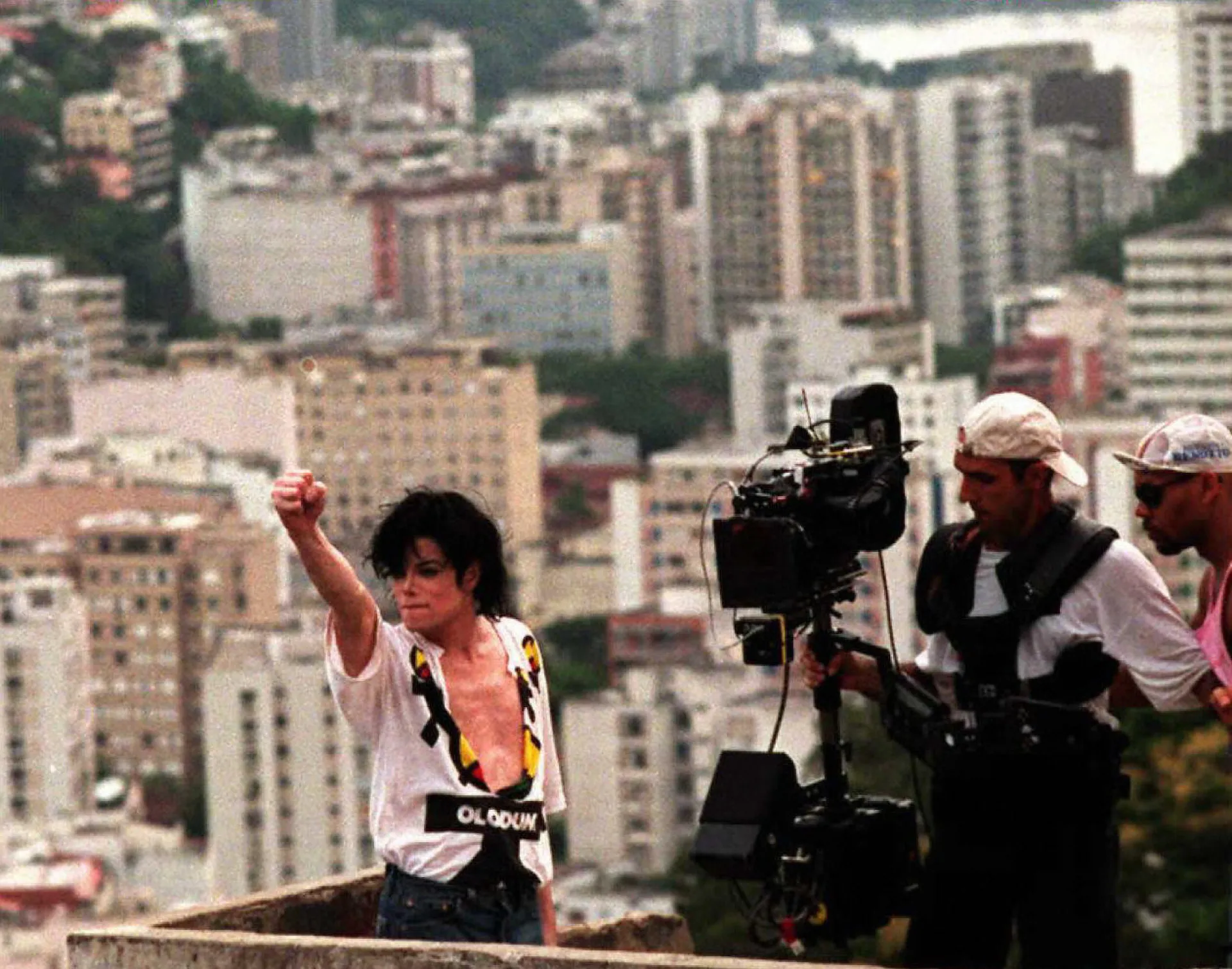 Michael Jackson sorrindo no Morro Dona Marta, com a cidade do Rio de Janeiro ao fundo.
