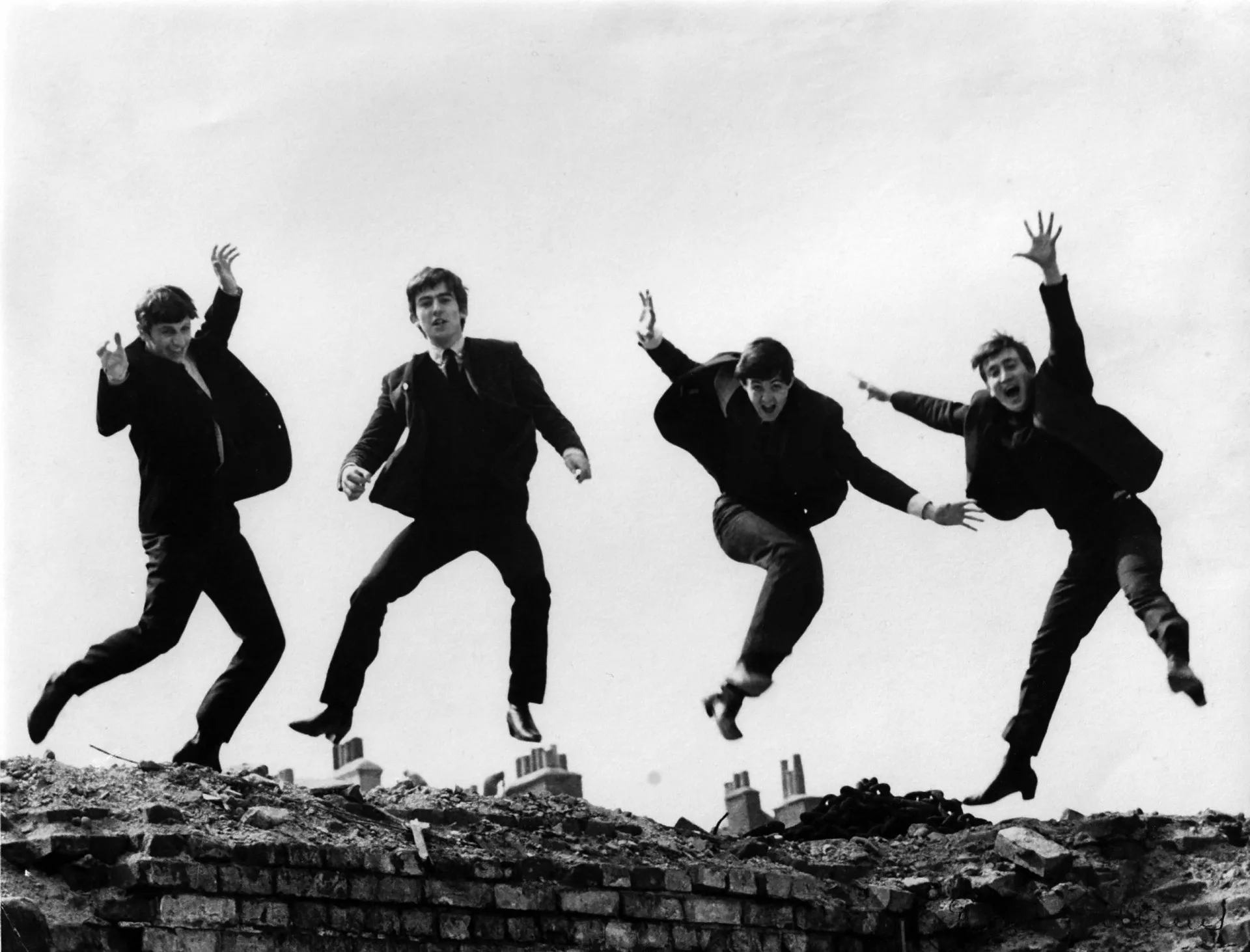 Os Beatles pulando no ar em um local bombardeado em Londres, com expressões alegres.