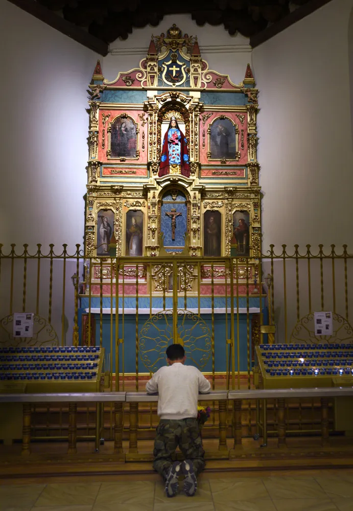 Uma pessoa rezando diante de um altar com várias imagens de santos.