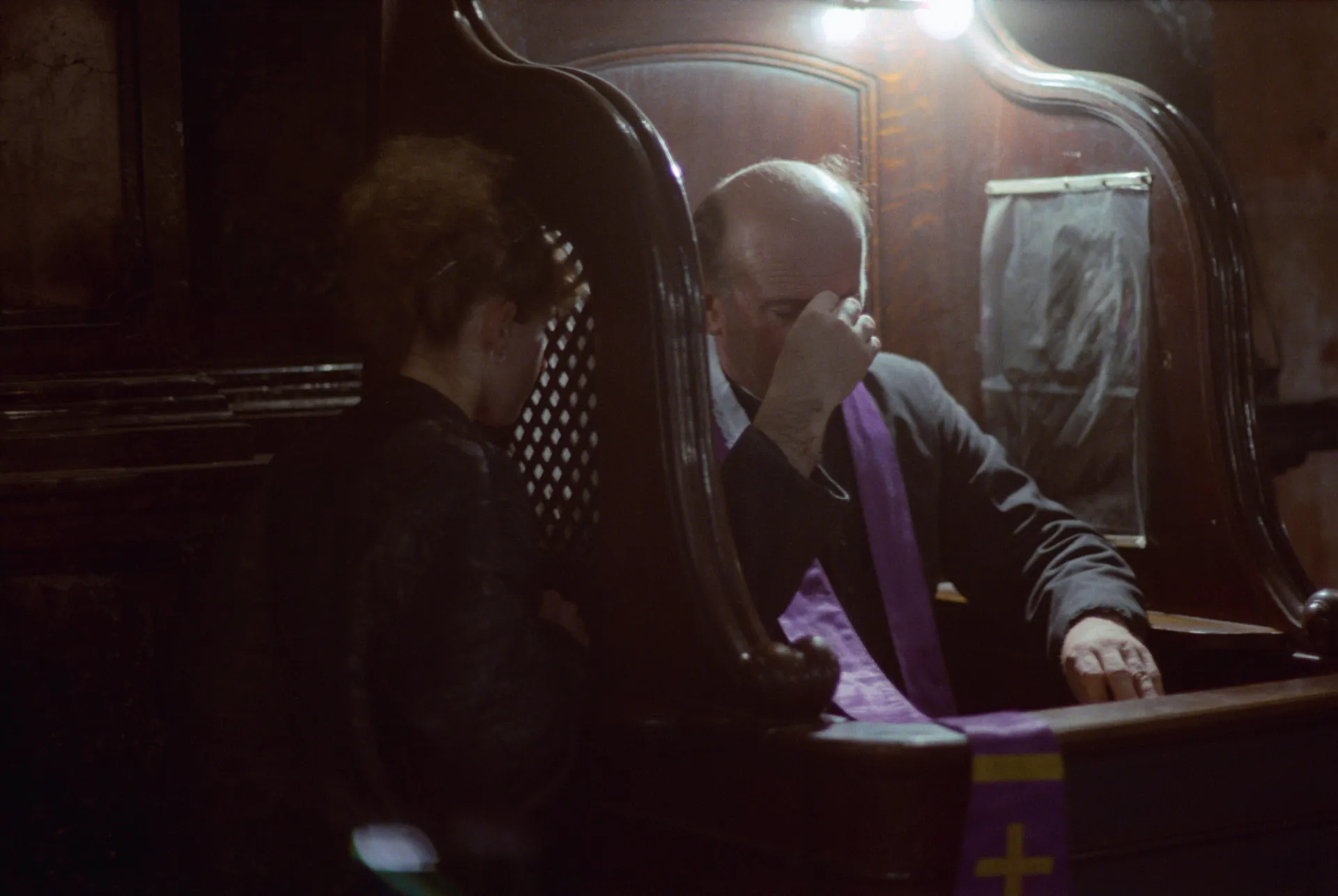 Uma pessoa se confessando a um padre em um confessionário tradicional.