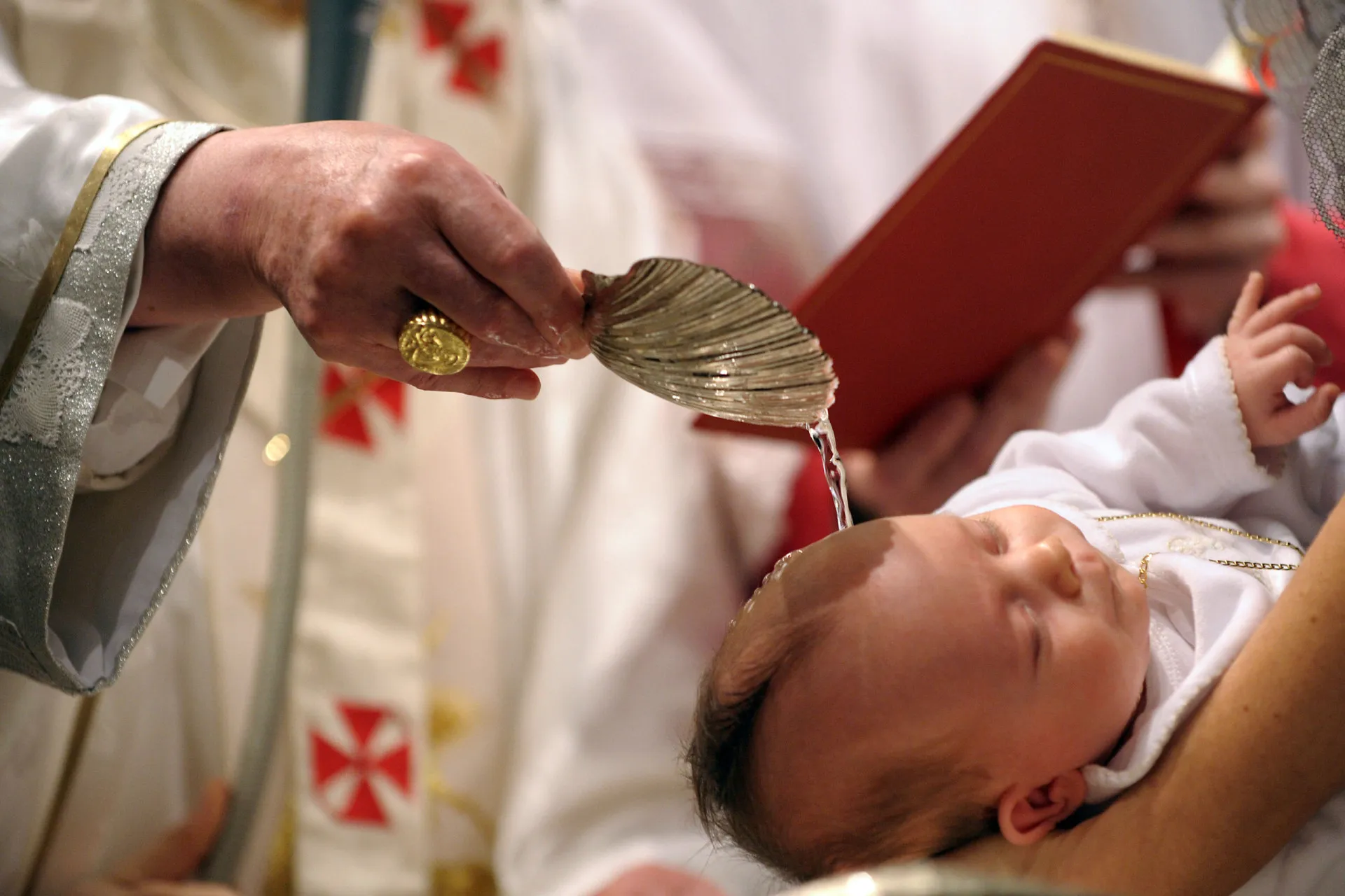 Um bebê sendo batizado com água por um padre em uma cerimônia católica.