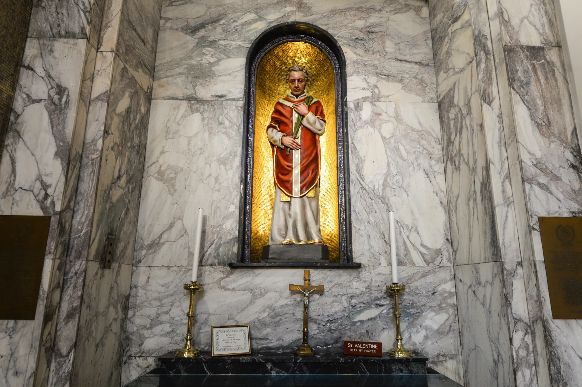 Uma estátua de um santo em uma igreja, com velas acesas por fiéis.