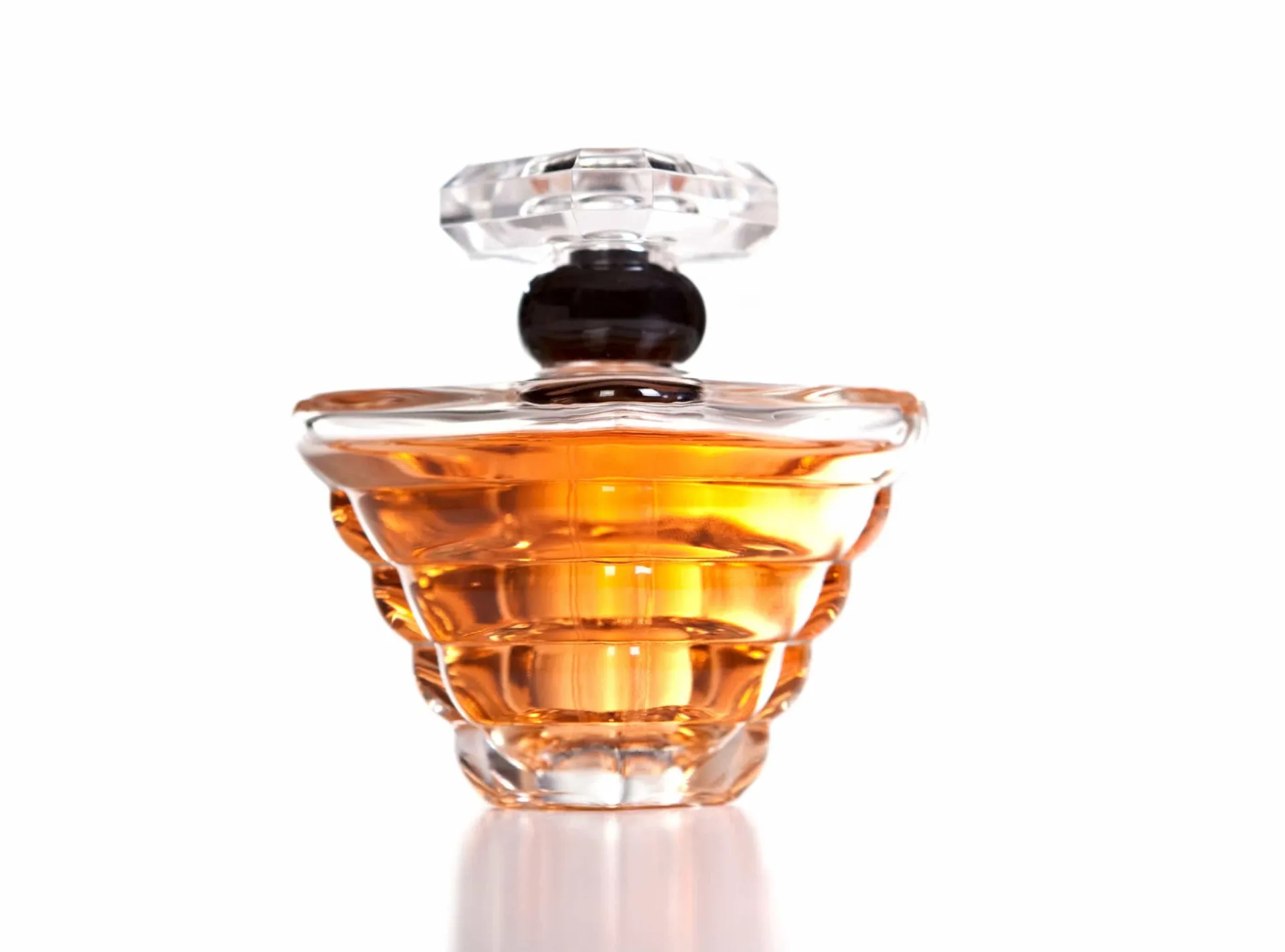 Frasco de perfume sobre uma base de madeira, cercado por folhas verdes.