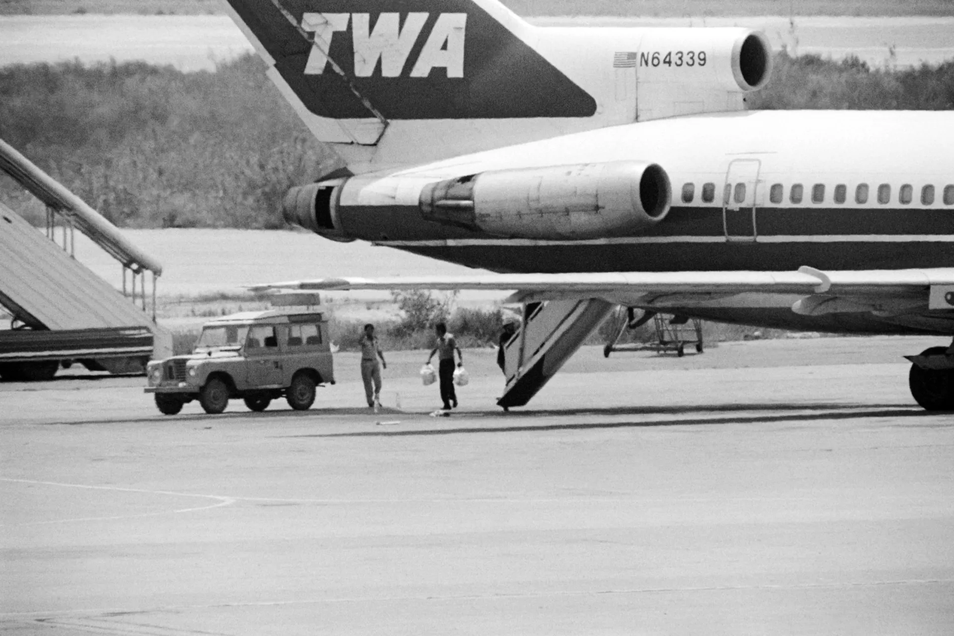 A aeronave do voo 847 da TWA parada na pista de um aeroporto, cercada por veículos de segurança.