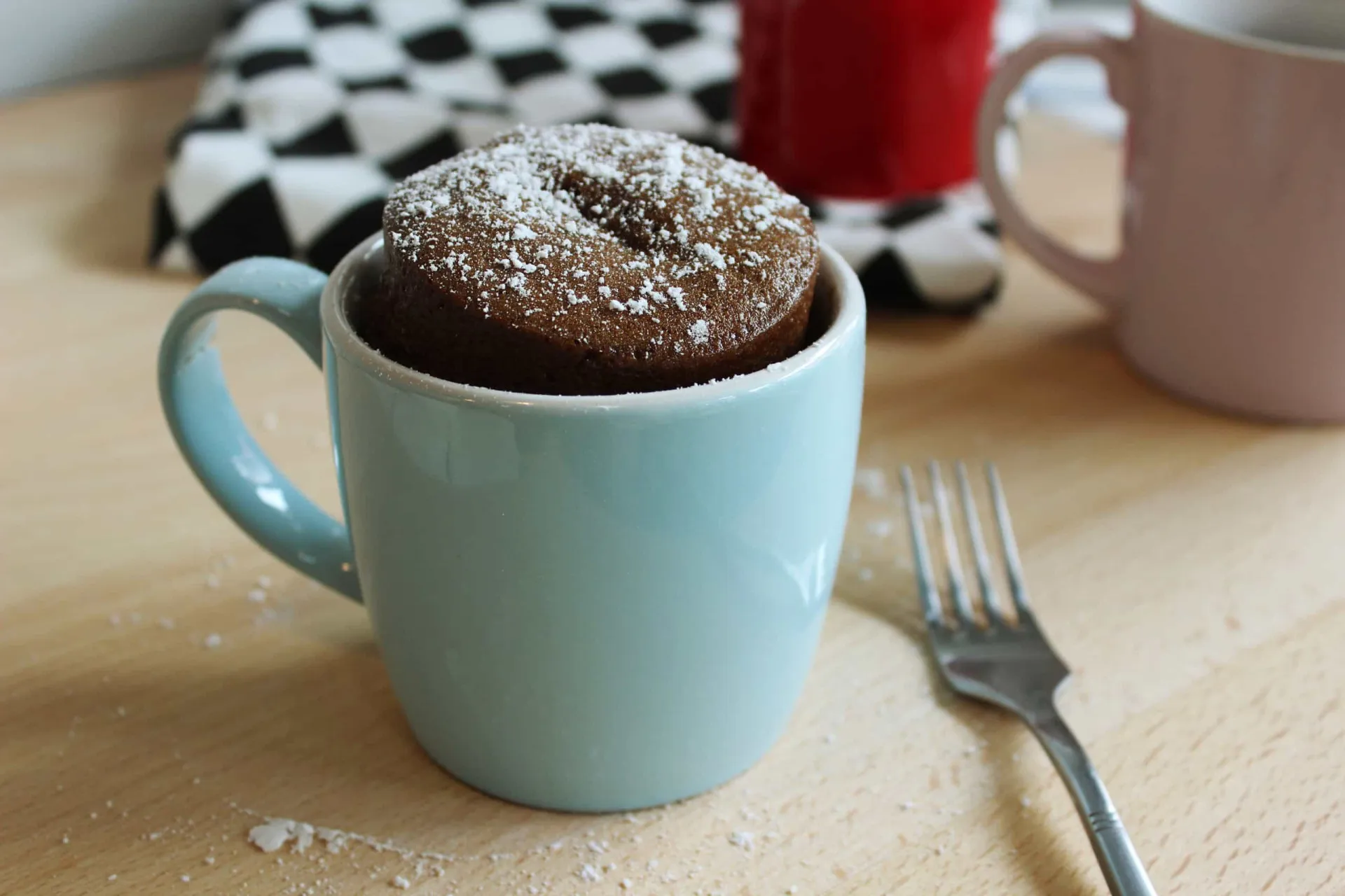 Um bolo de chocolate fofinho crescendo para fora de uma caneca, recém-saído do micro-ondas.