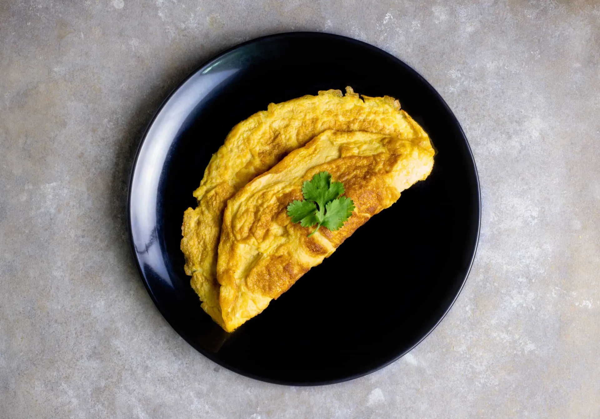 Omelete dourado e fofo sendo dobrado ao meio em uma frigideira.