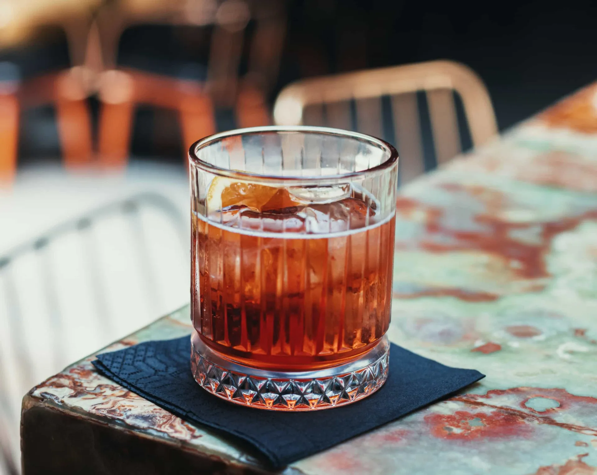 Copo baixo com um Negroni de cor vermelha vibrante, gelo grande e uma fatia de casca de laranja.