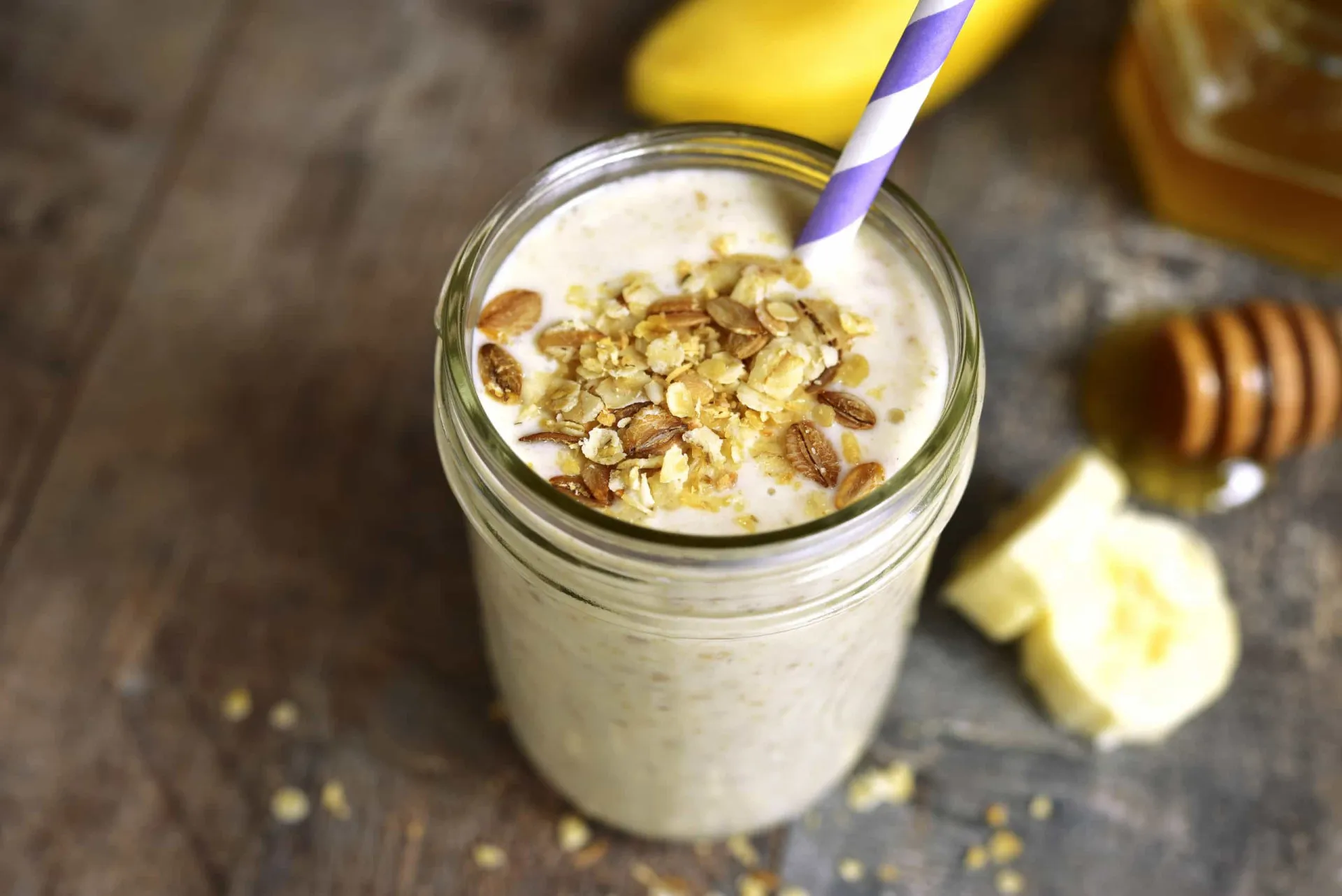 Copo de smoothie cremoso de banana e aveia, com bananas e aveia ao lado.