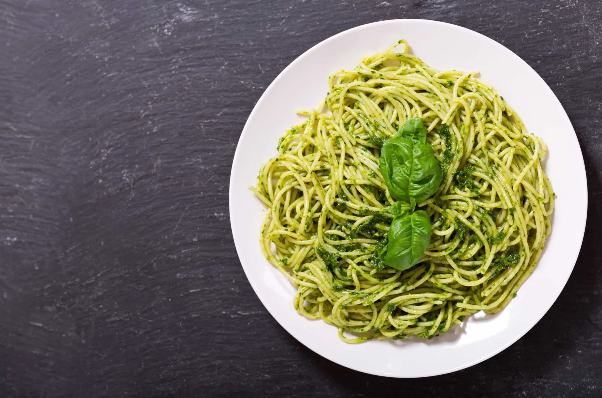 Prato de espaguete envolto em um vibrante molho pesto verde e coberto com queijo parmesão ralado.