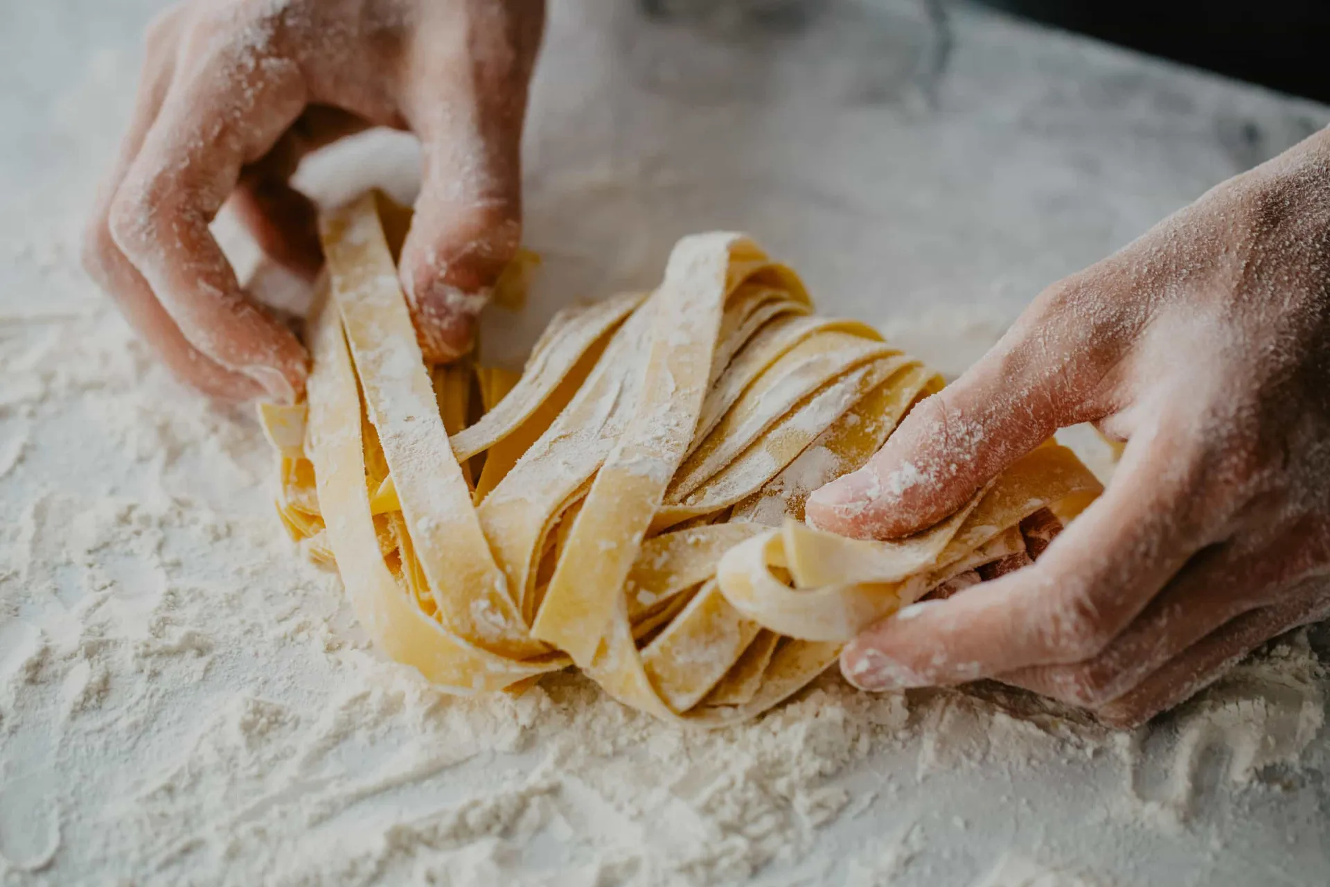 Massa de macarrão fresca sendo cortada em tiras finas por uma máquina de macarrão.