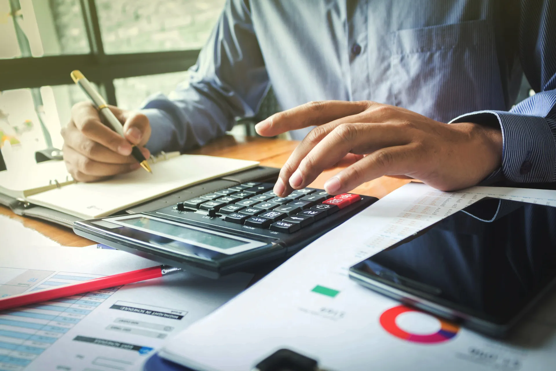 Uma pessoa usando uma calculadora e analisando gráficos financeiros em um escritório.