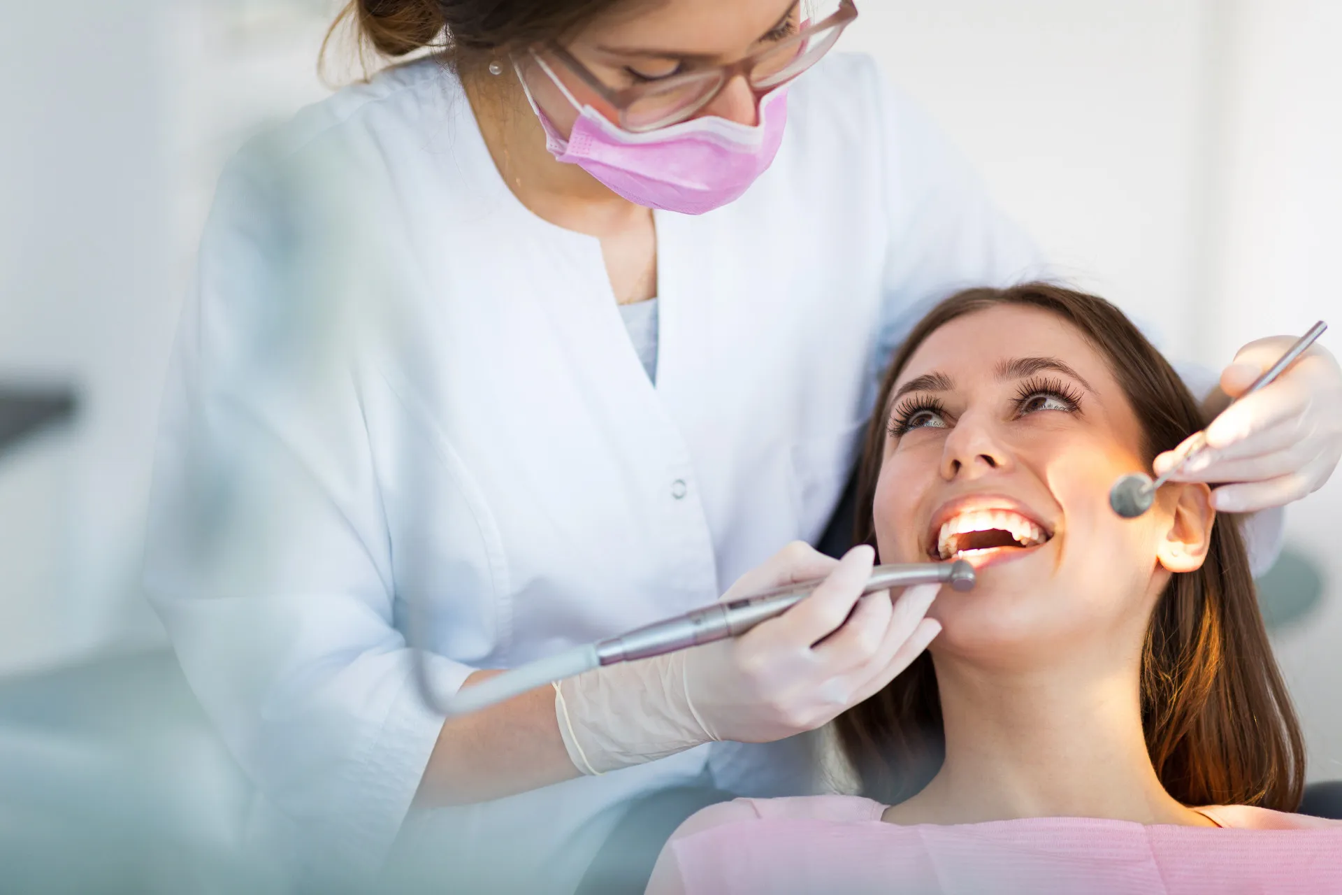 Um dentista sorridente realizando um procedimento em um paciente em sua cadeira.