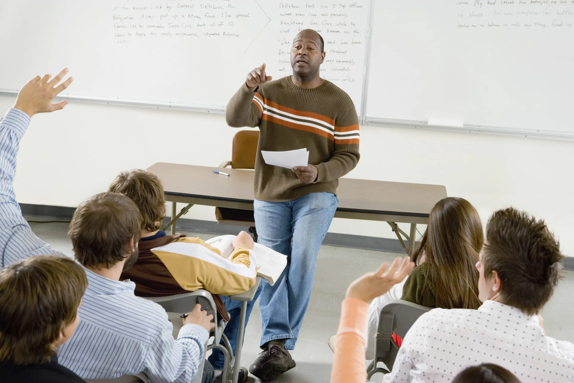 Um professor universitário dando aula em um auditório, interagindo com os alunos.