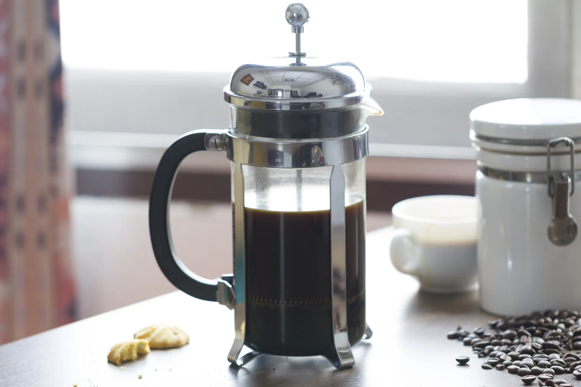 Xícara de café preto em uma mesa de madeira, com grãos de café espalhados ao redor.