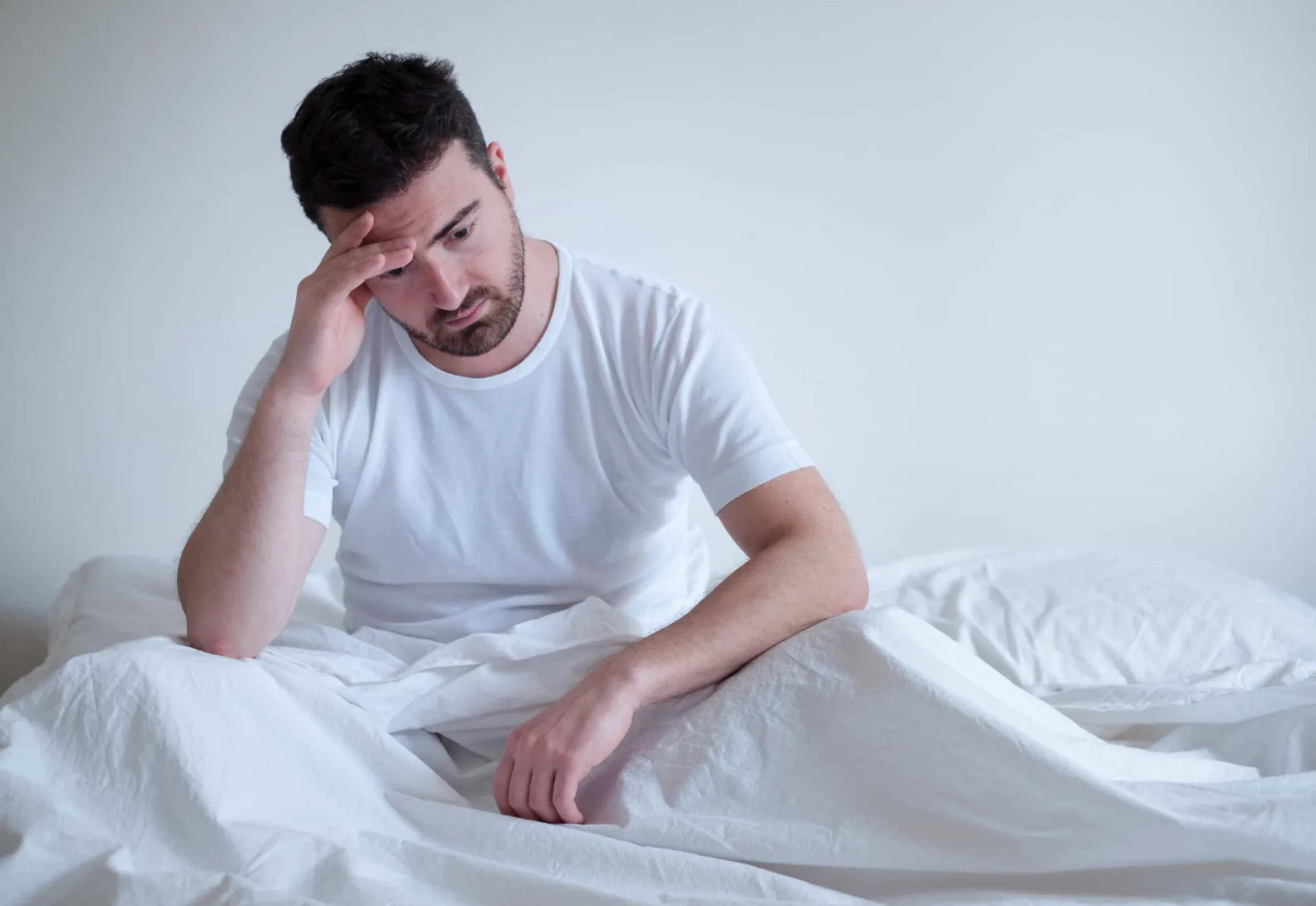 Um casal na cama, com o homem parecendo preocupado e distante.