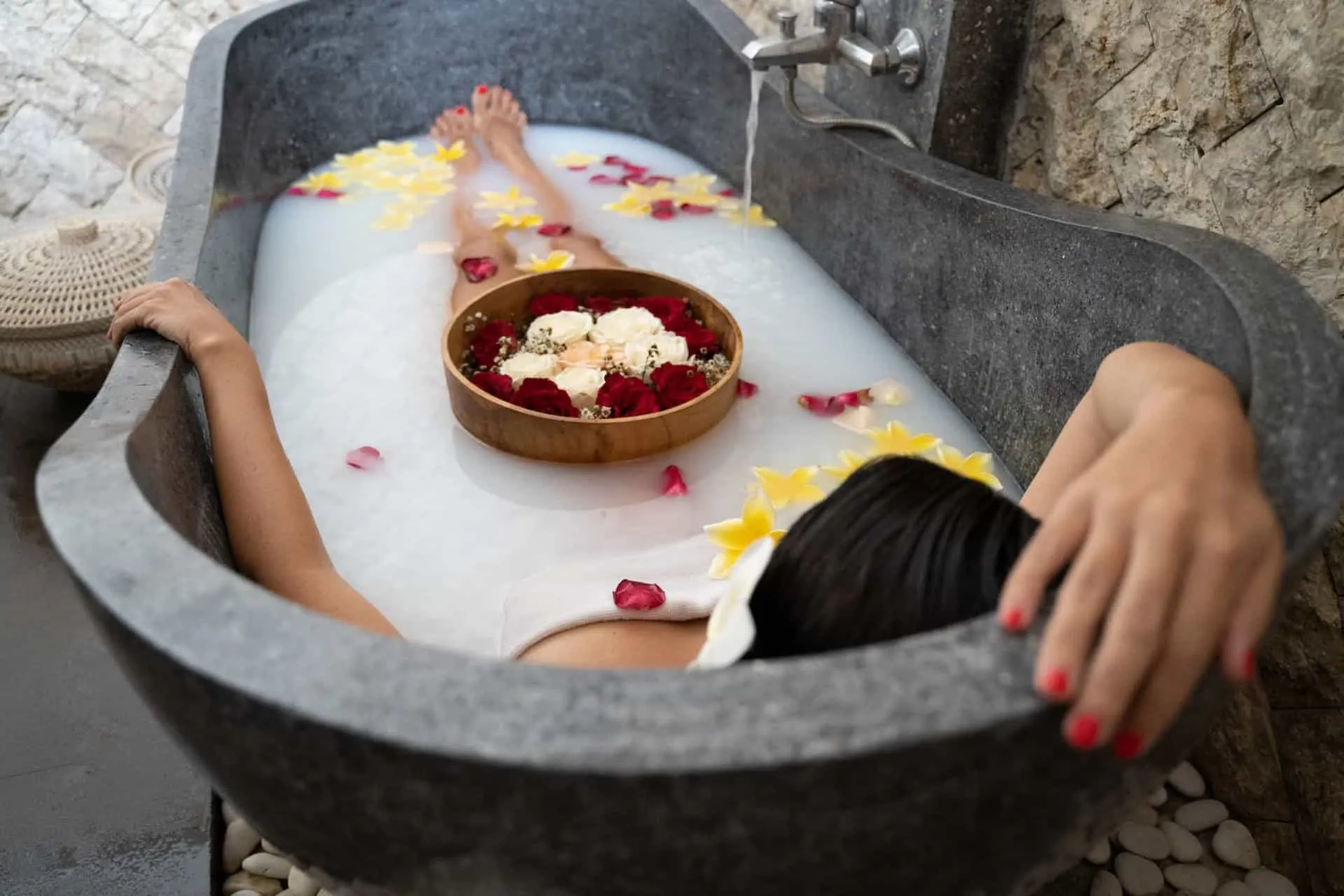 Pés de uma pessoa relaxando em uma banheira com espuma e pétalas de flores.