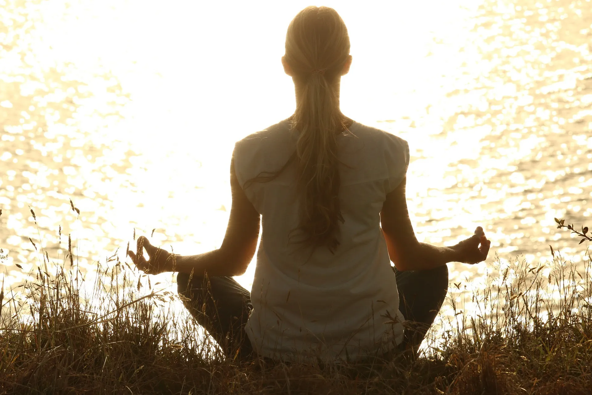 Uma pessoa meditando na beira de um lago calmo ao amanhecer.