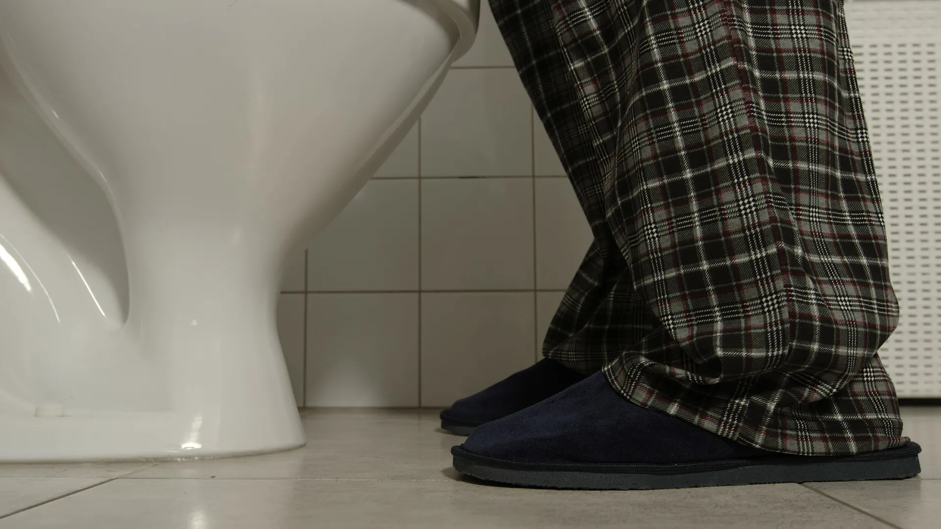 Pessoa sentada na beira da cama, contemplativa, após acordar mais uma vez para urinar.