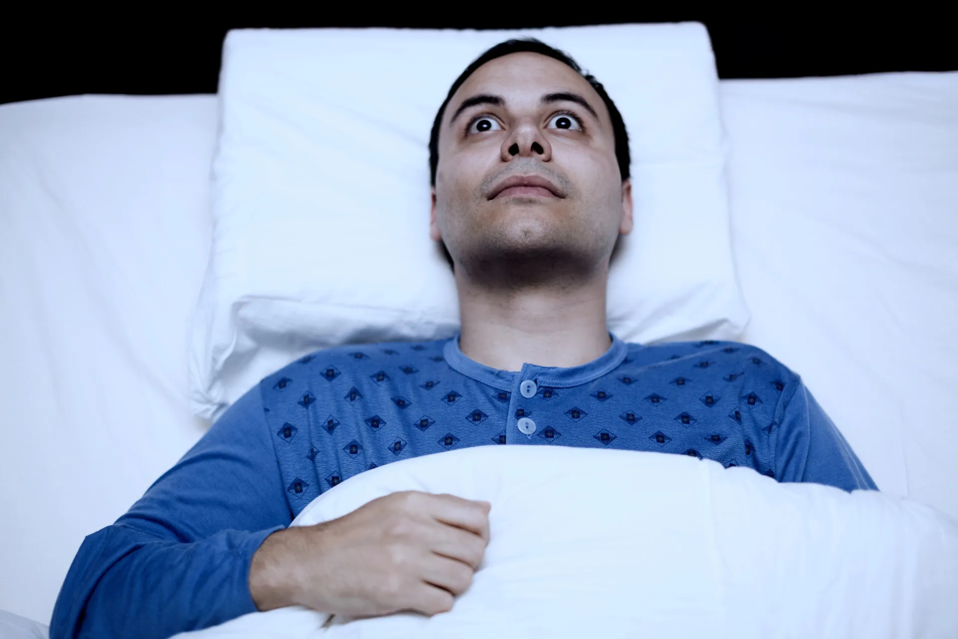 Mulher idosa sentada na cama, parecendo cansada por ter acordado durante a noite.