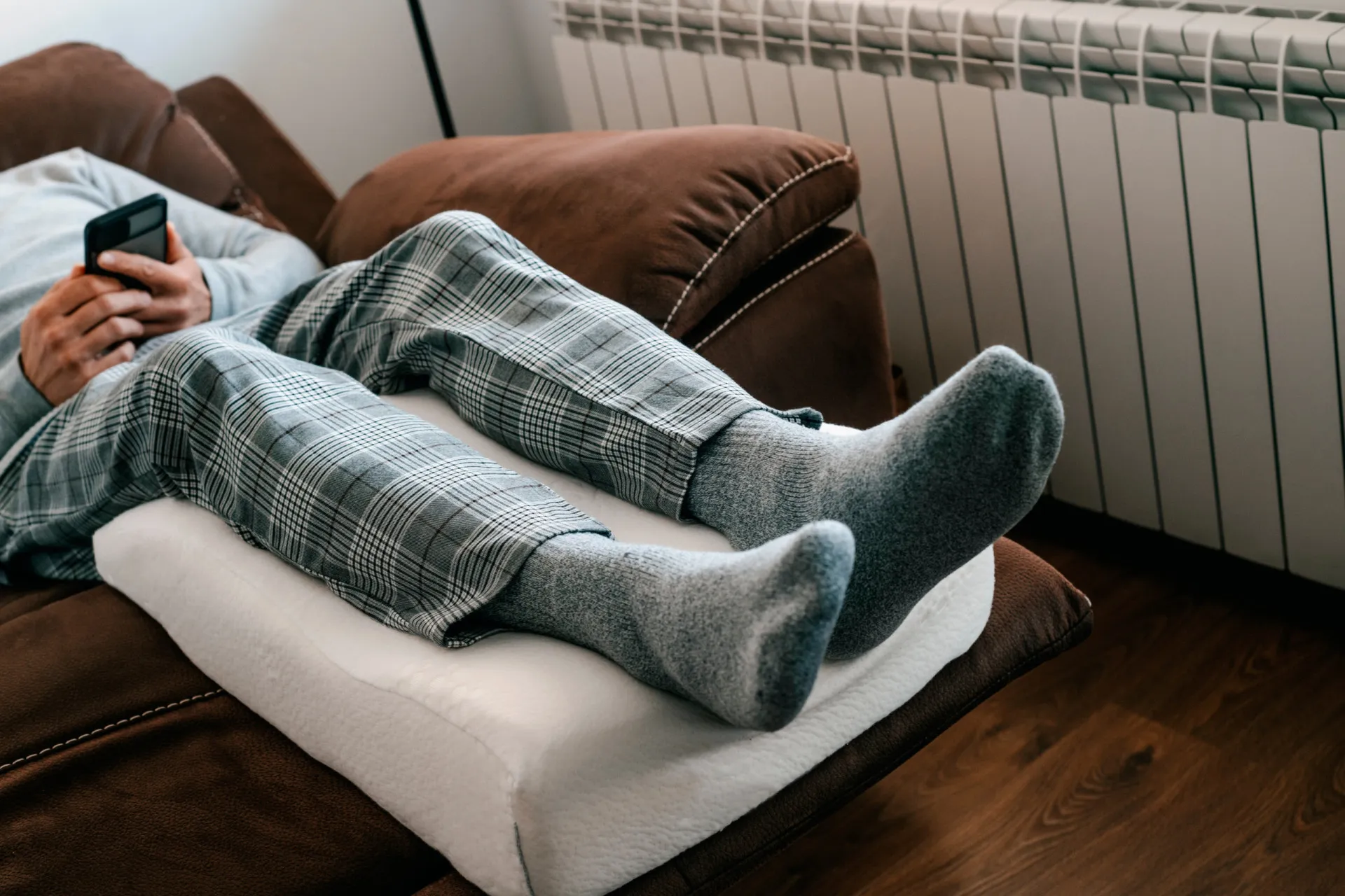 Pessoa deitada na cama com as pernas elevadas e apoiadas na parede.