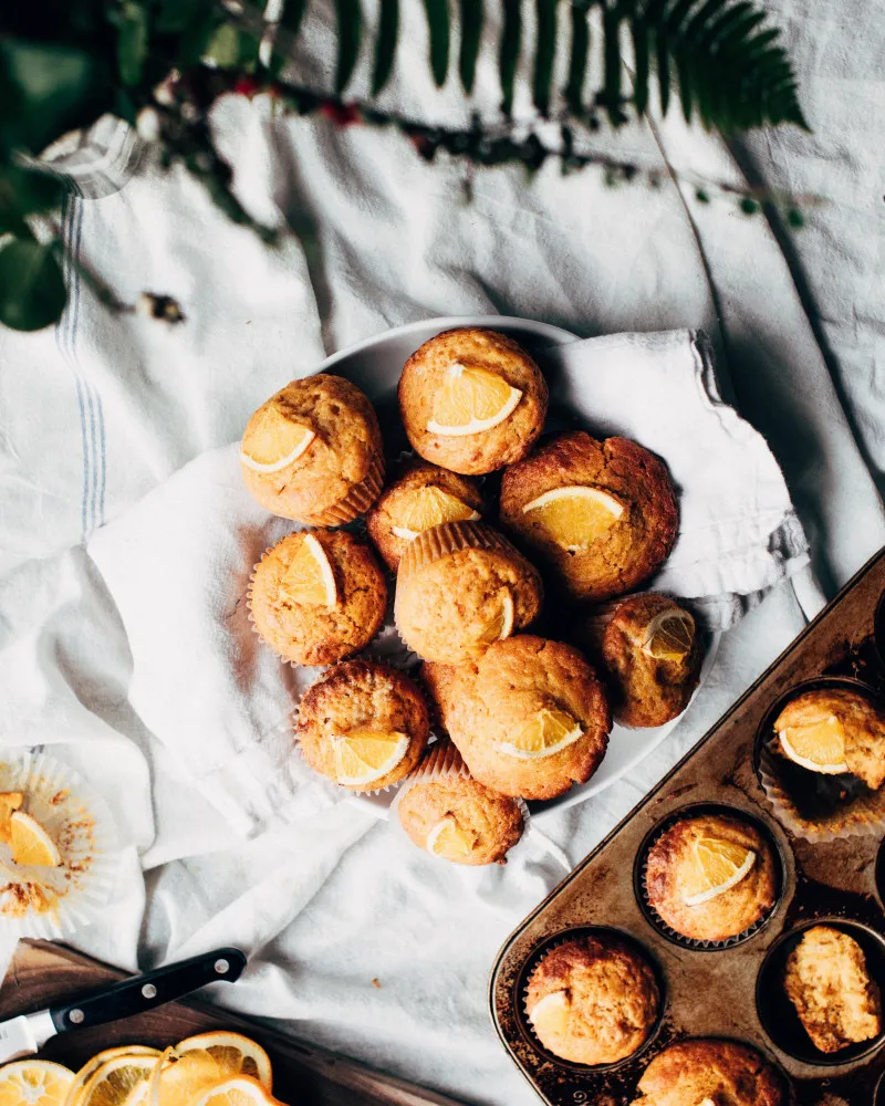 Bolinhos caseiros de laranja com uma cobertura de glacê branco e raspas de laranja.