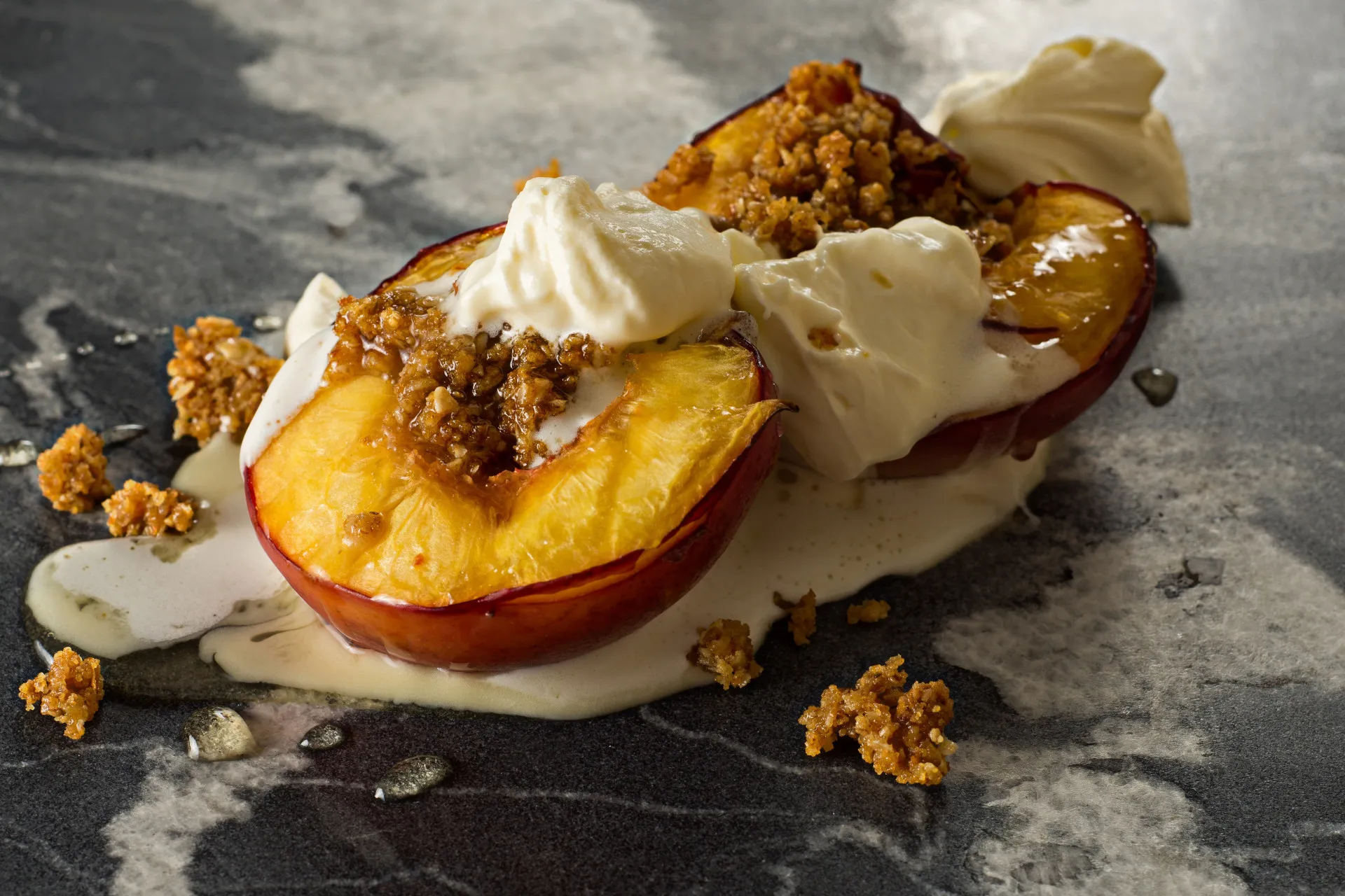 Nectarinas assadas servidas com farofa de biscoito, chantilly e um fio de mel.