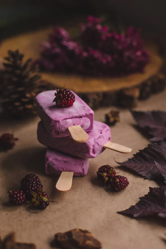 Picolés caseiros de iogurte com frutas vermelhas inteiras visíveis.