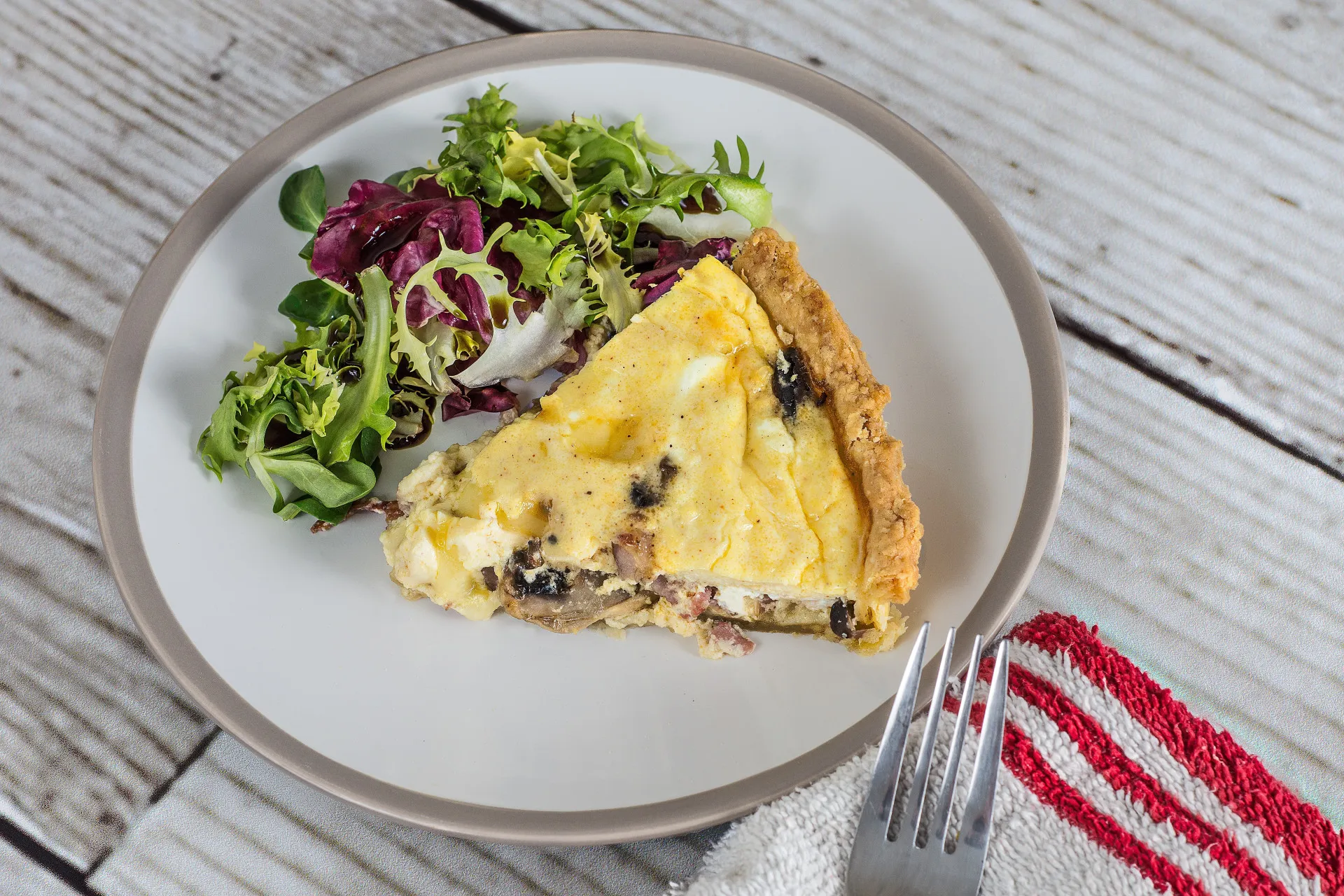 Fatia de quiche caseira ao lado de uma salada de folhas verdes em um prato.