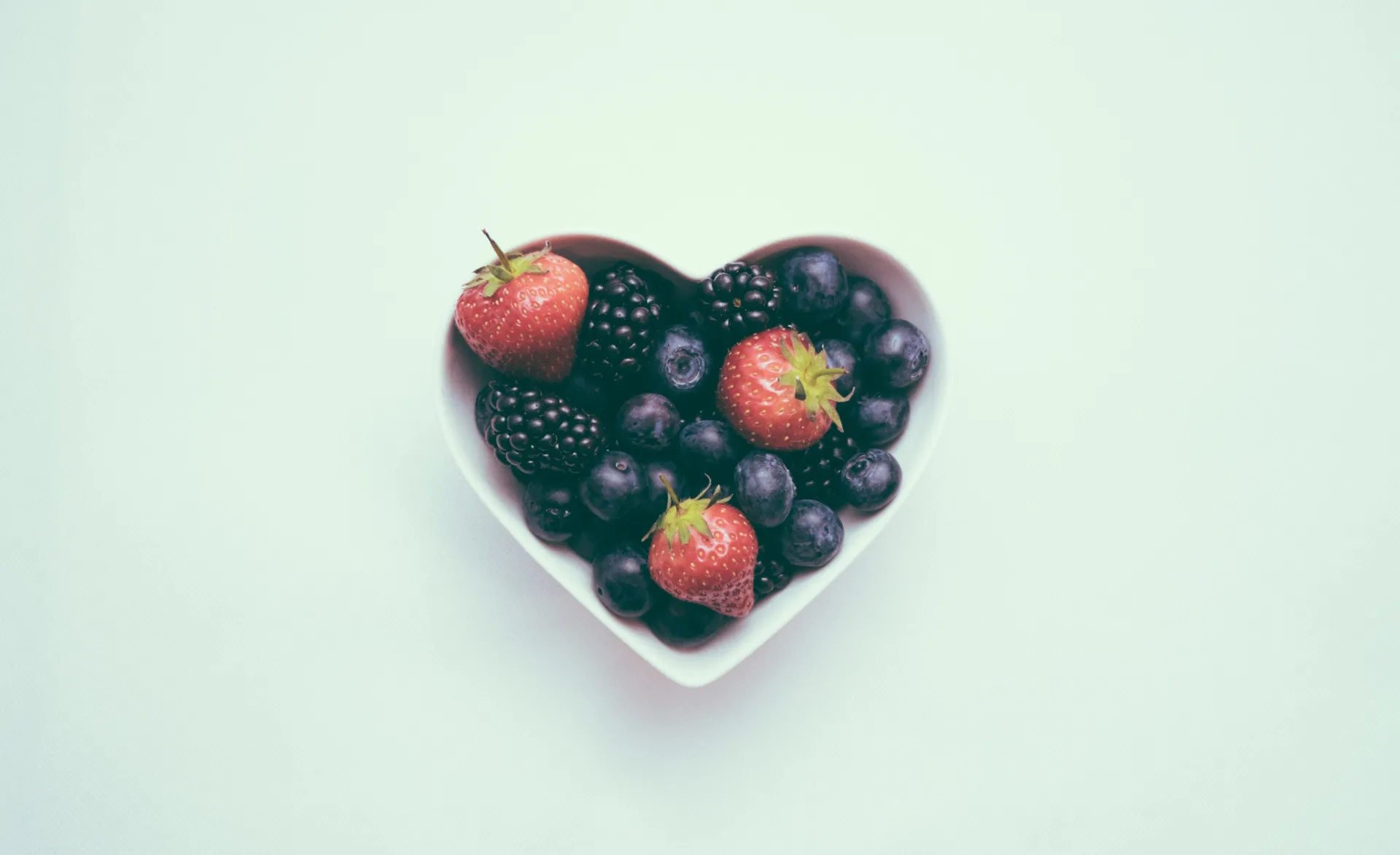 Tigela em formato de coração cheia de frutas silvestres frescas como mirtilos e framboesas.