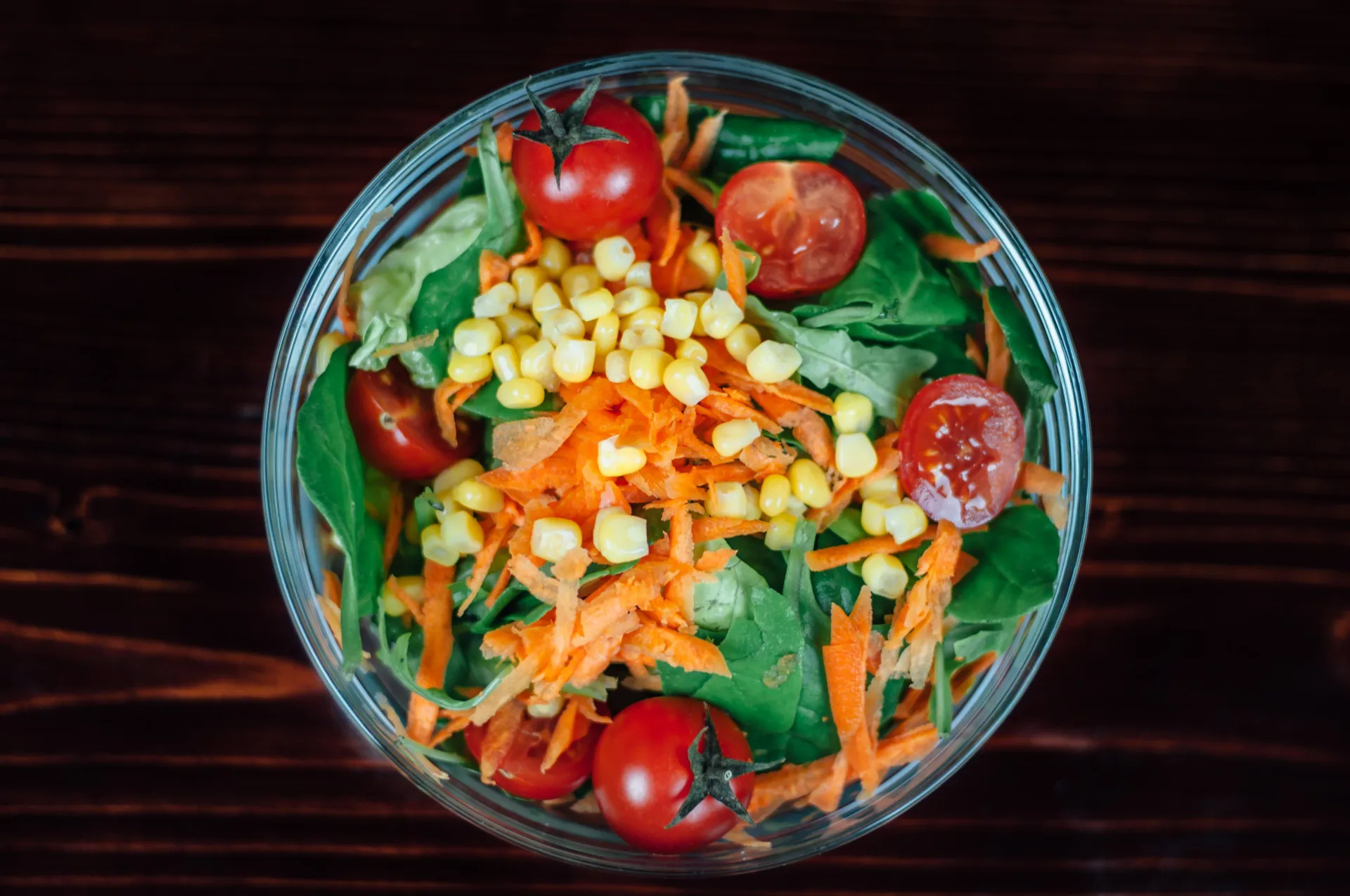 Tigela de salada extremamente colorida, com folhas, vegetais e frutas de várias cores.
