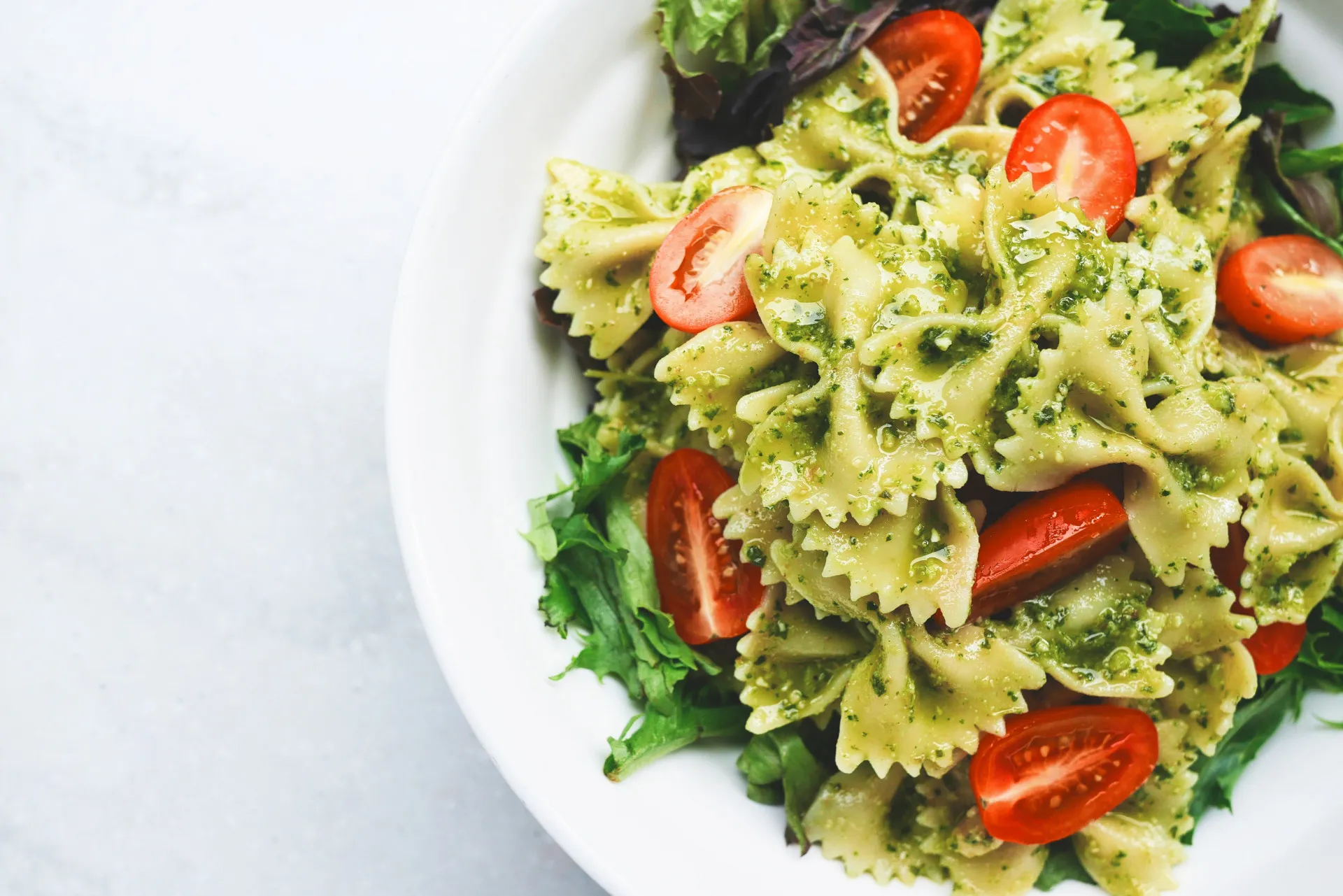 Prato de massa tipo penne coberto com um vibrante e fresco molho pesto verde.