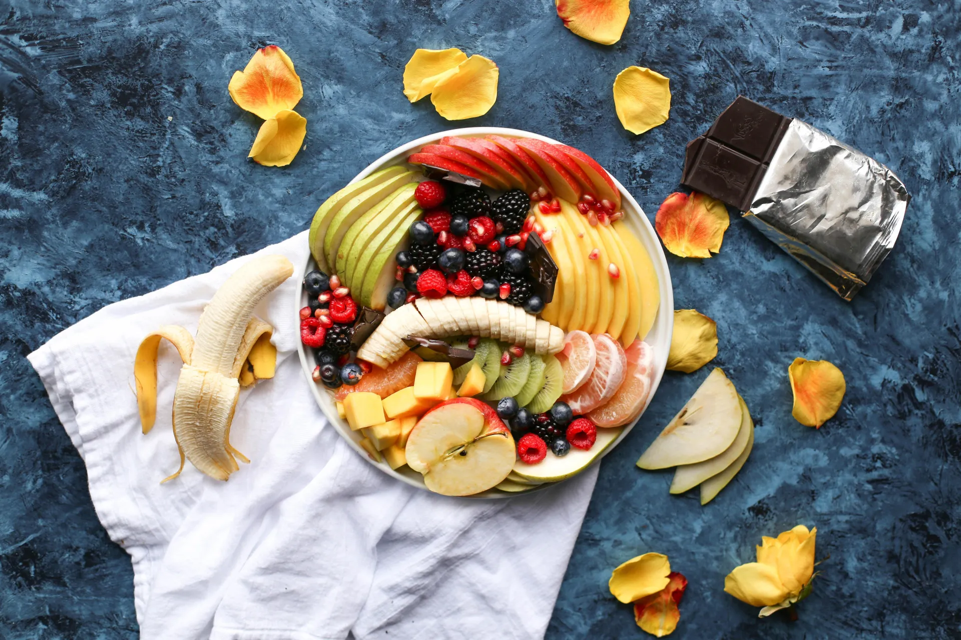 Tigela branca cheia de frutas frescas fatiadas, como morango, kiwi e manga.
