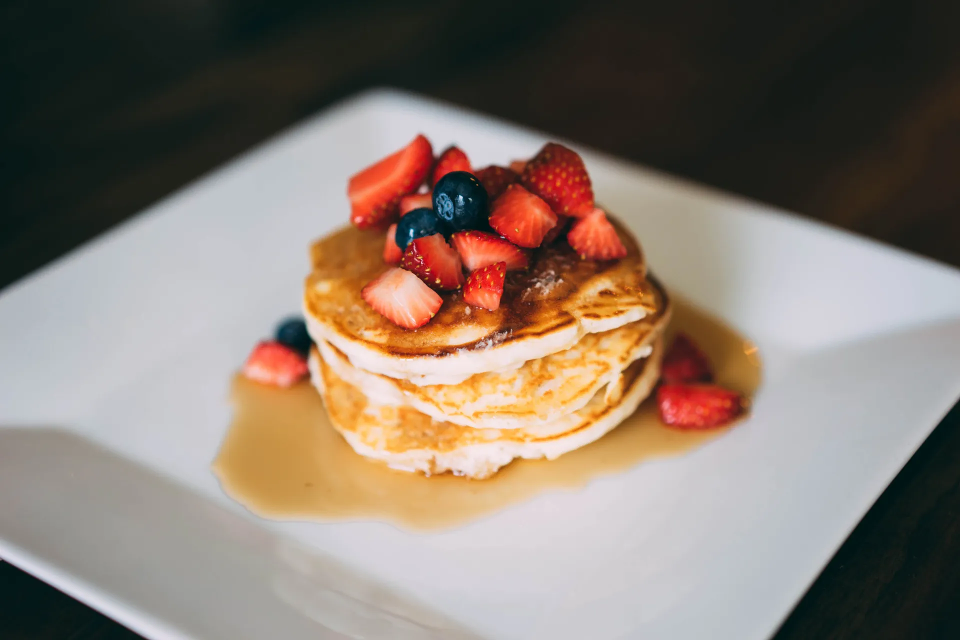 Pilha alta de panquecas americanas fofas, cobertas com frutas vermelhas e mel.