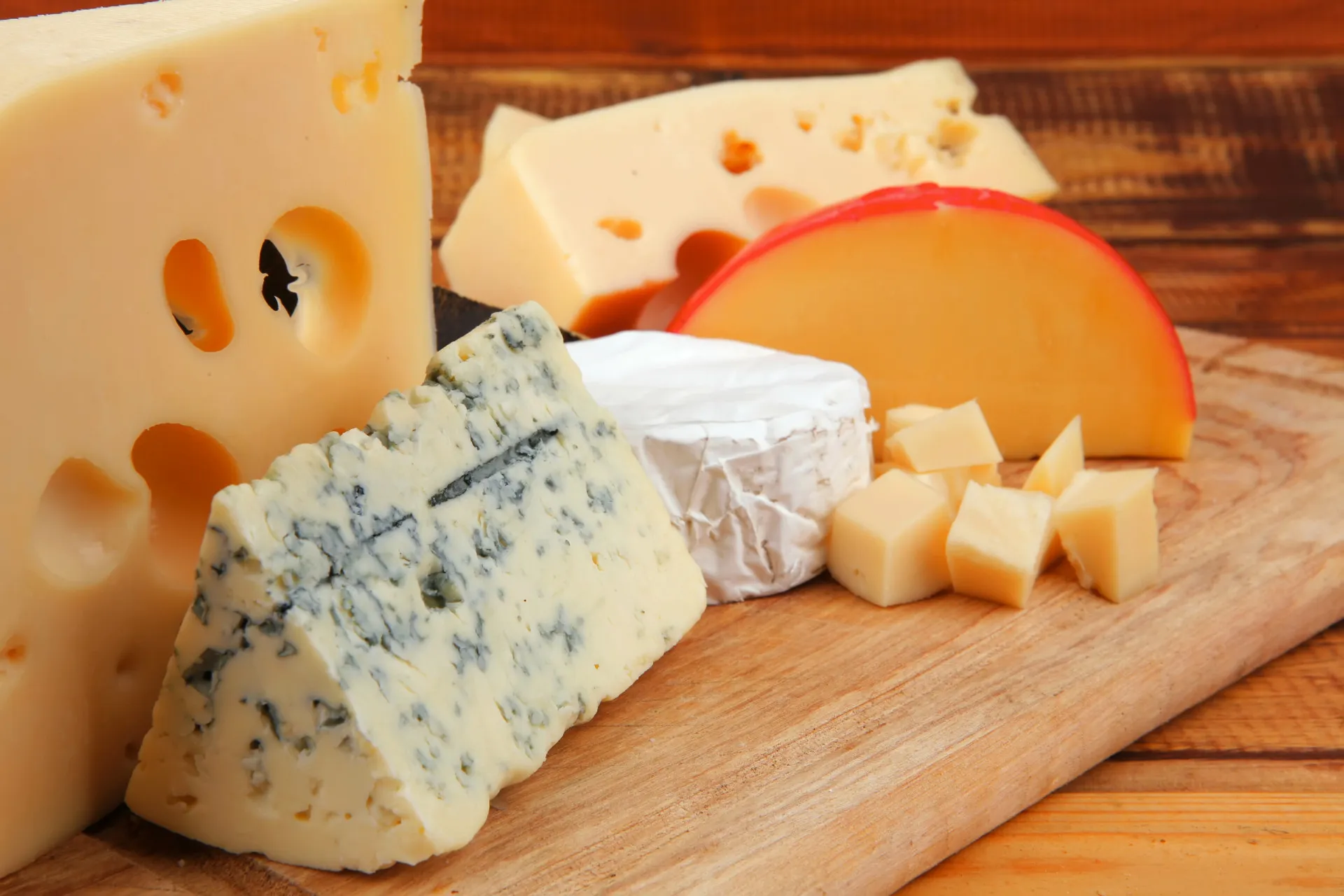 Pedaços variados de queijos envelhecidos, como parmesão e gorgonzola, em uma tábua.