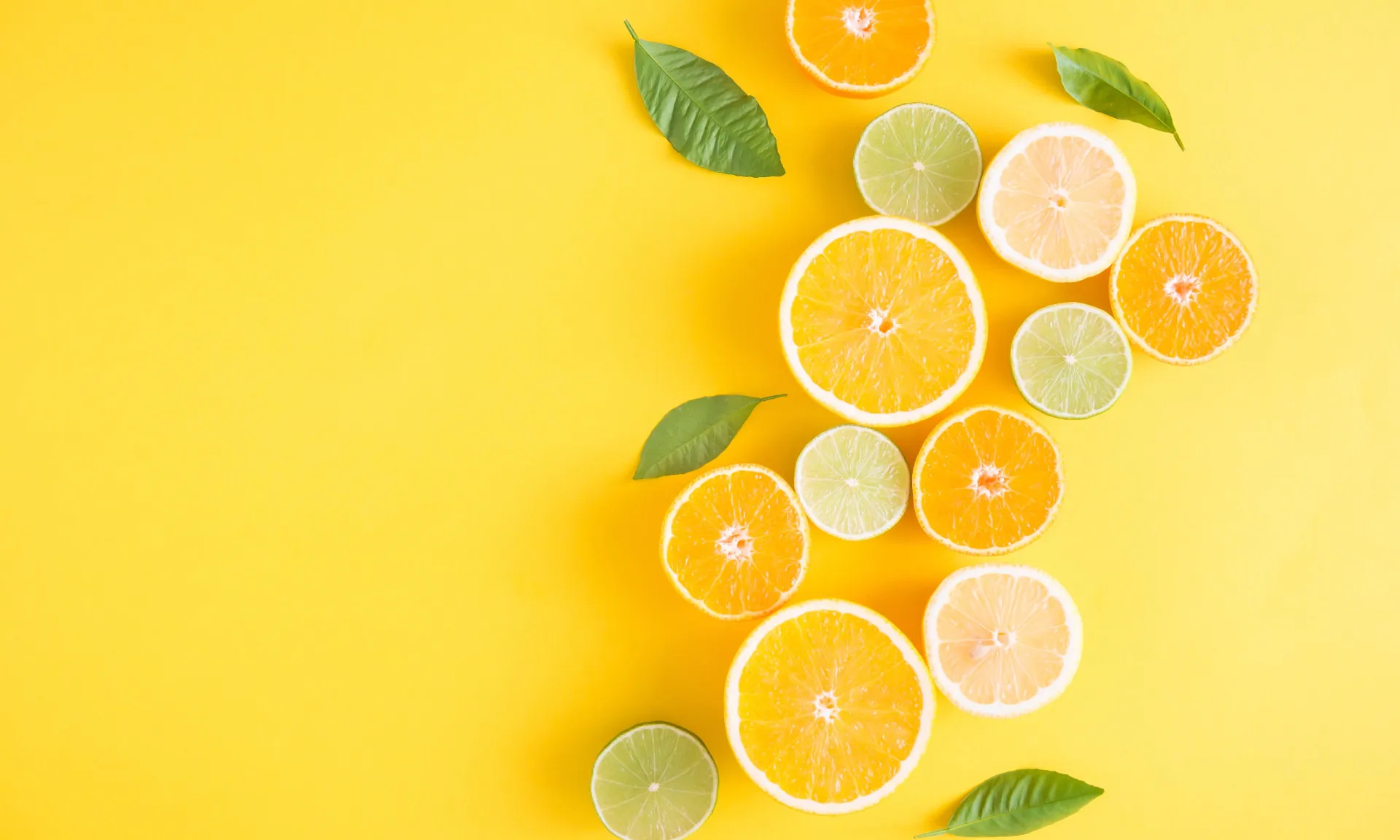 Um copo de suco de laranja fresco ao lado de laranjas inteiras e fatiadas.