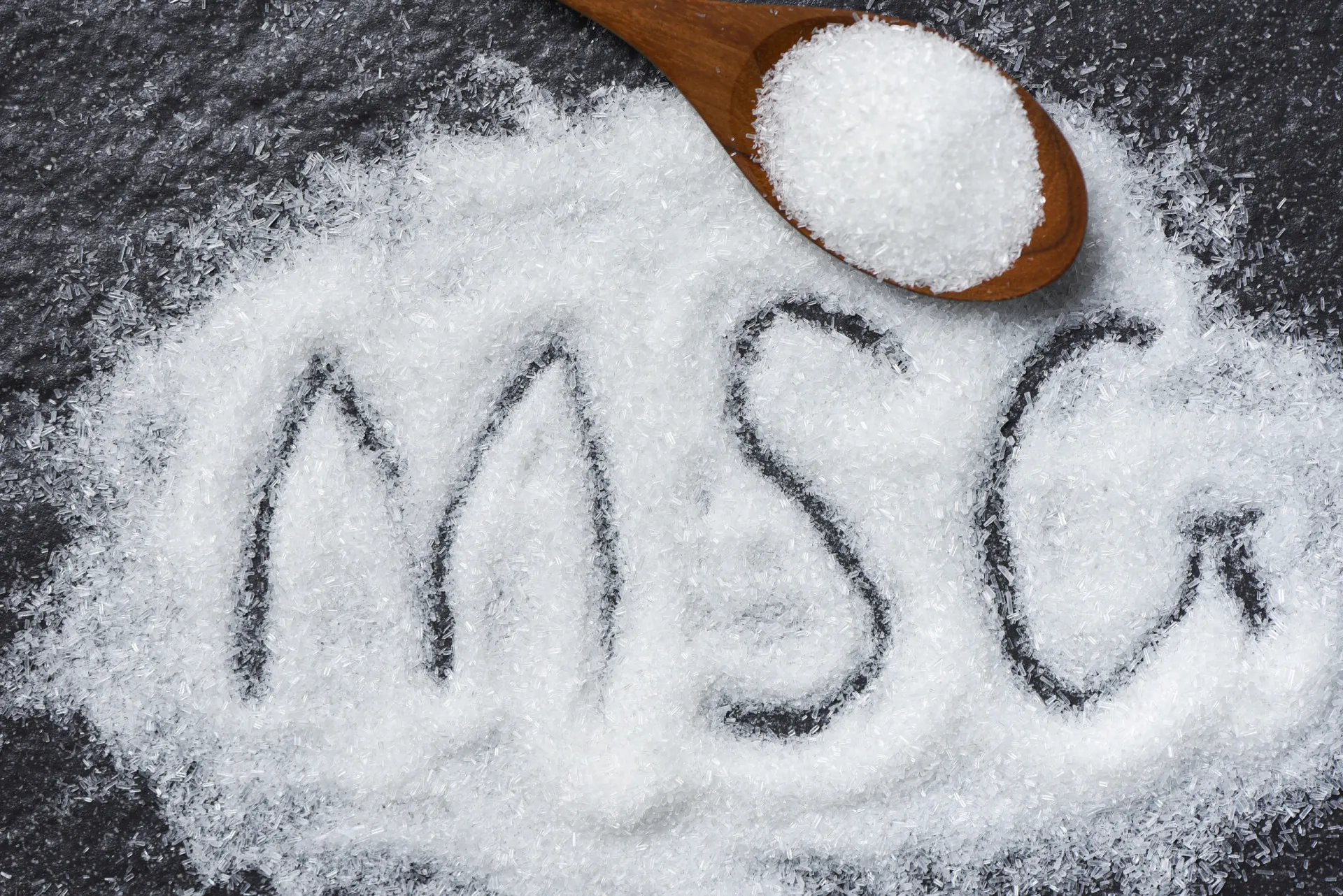 Pó branco de glutamato monossódico (MSG) em uma colher de madeira.