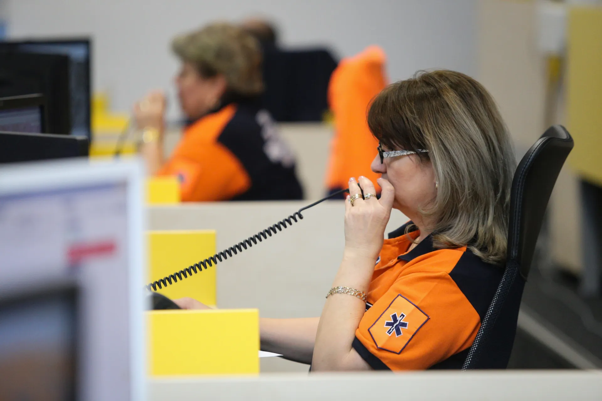 Operador de emergência falando ao telefone com fone de ouvido, em um centro de controle.