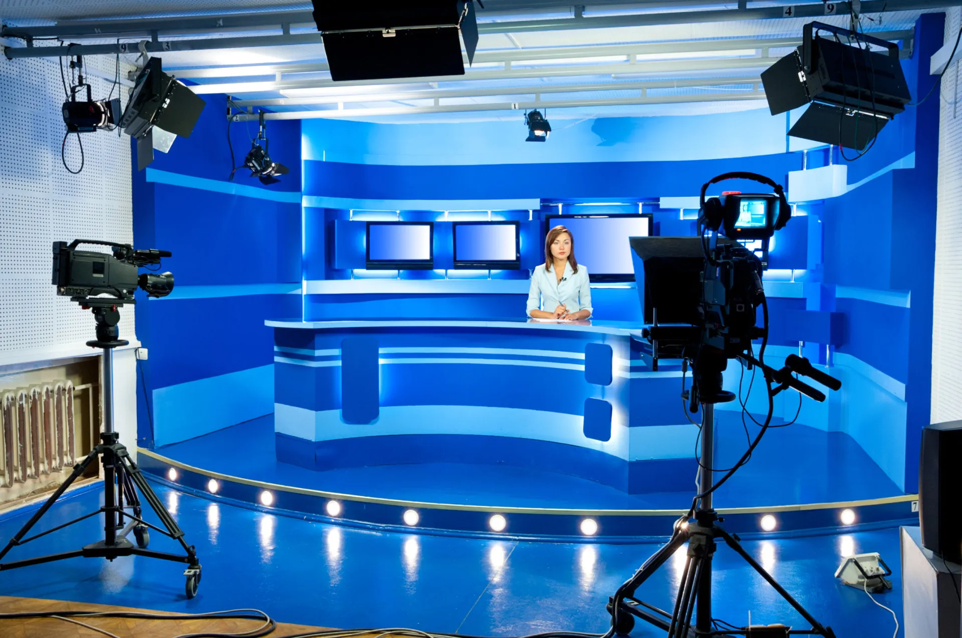 Apresentadora de TV em uma bancada de noticiário, falando para a câmera.