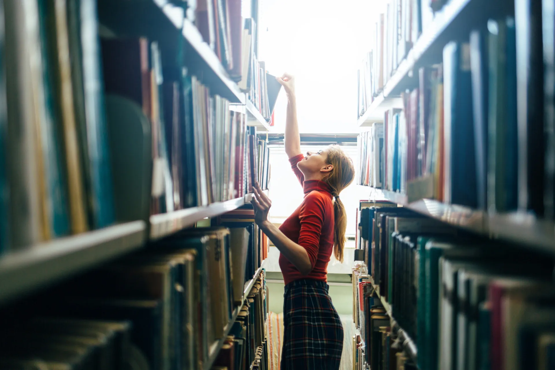 Bibliotecário em um ambiente silencioso e imponente de uma biblioteca, rodeado por estantes de livros.