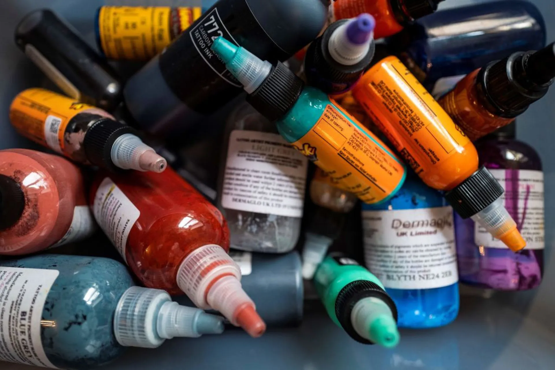 Frascos de tinta de tatuagem colorida alinhados em uma prateleira de estúdio.