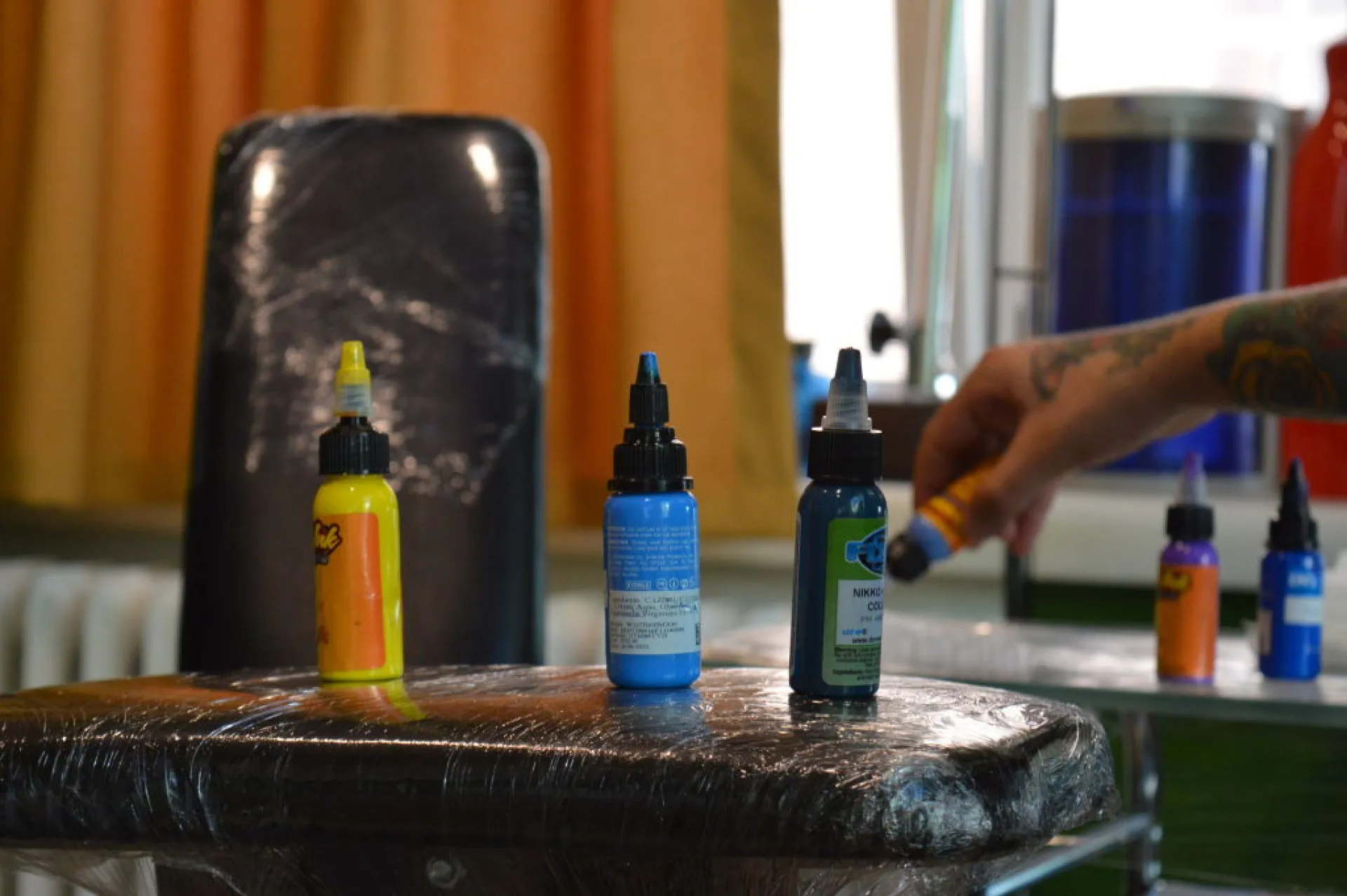 Mãos enluvadas de um tatuador preparando a tinta em pequenos copos descartáveis.