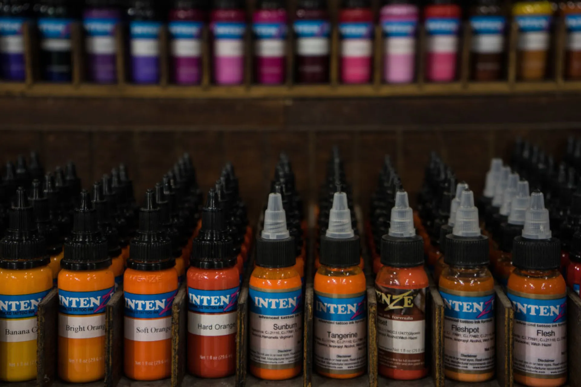 Vários frascos de tinta de tatuagem guardados em uma gaveta escura e organizada.