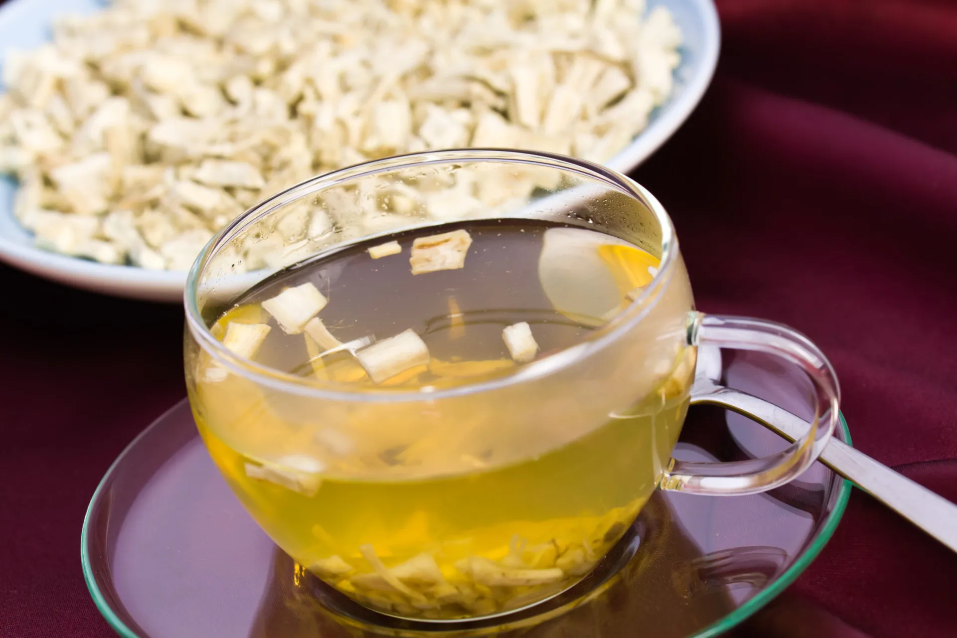 Chá de raiz de marshmallow em uma xícara de vidro, com as raízes secas ao lado para infusão.