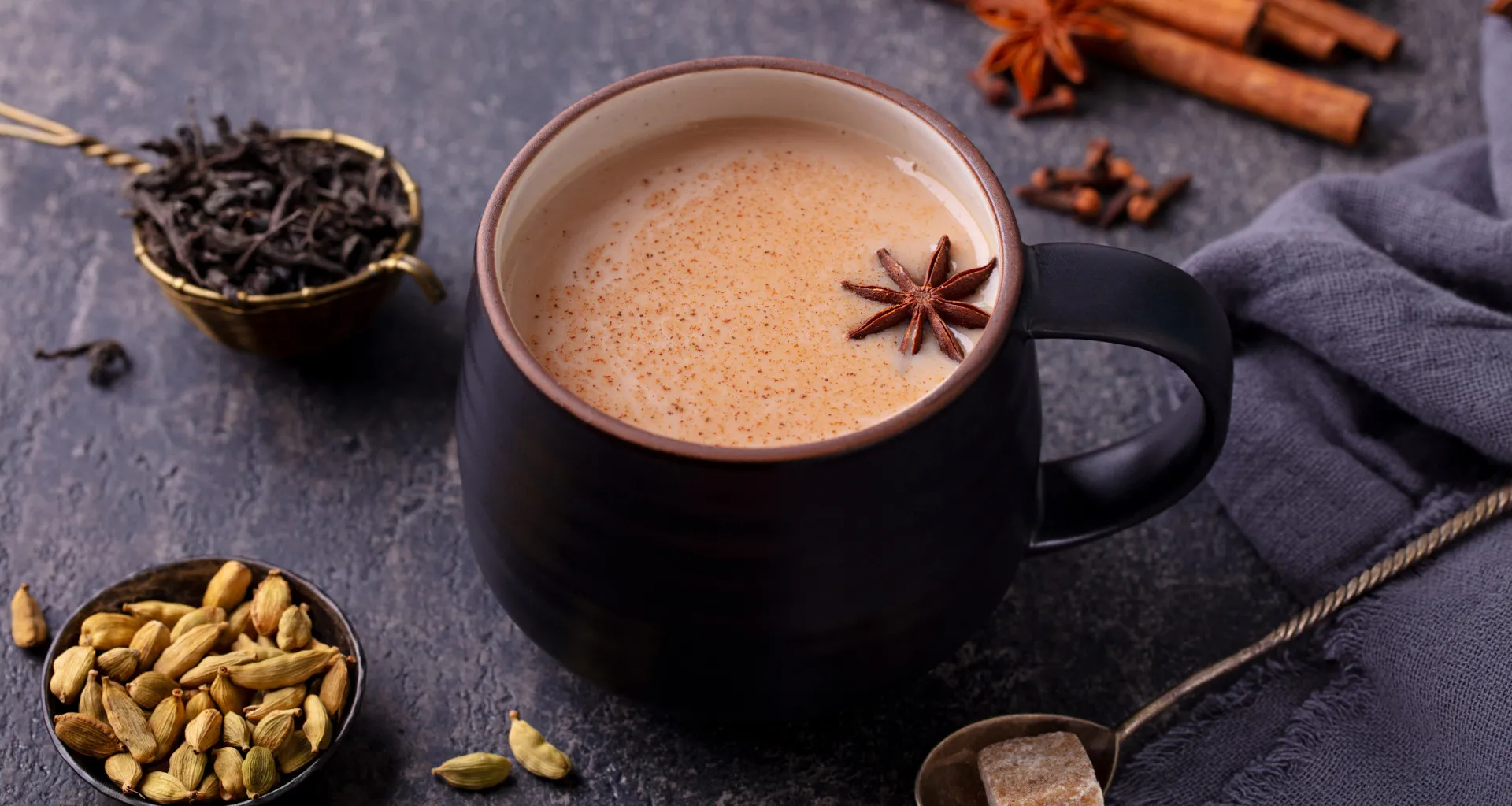 Xícara de masala chai cremoso com especiarias como canela e anis estrelado ao lado.