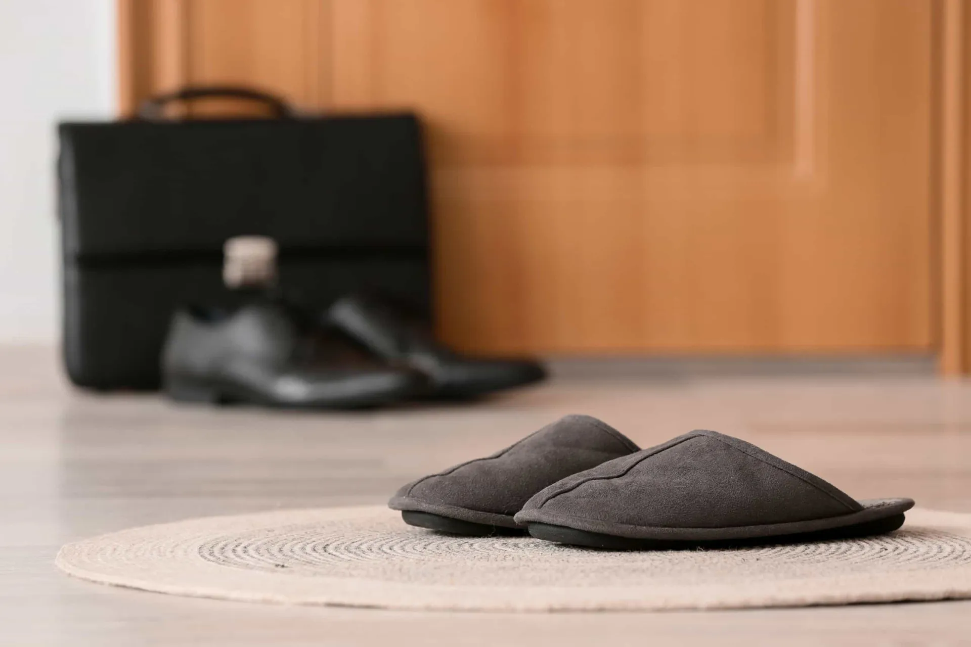 Par de pantufas felpudas estrategicamente posicionado ao lado de uma cama em um piso de madeira.