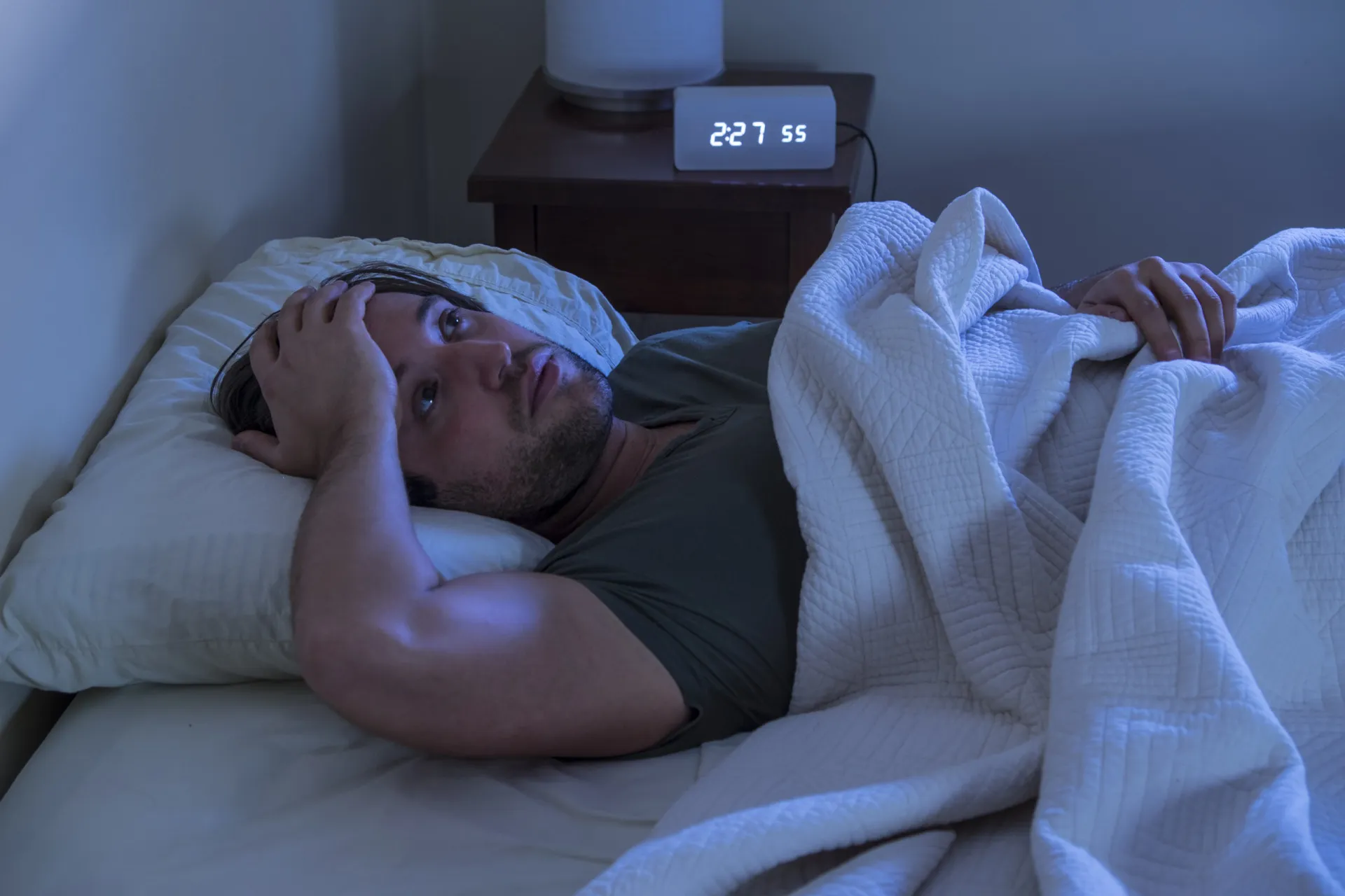 Pessoa na cama de olhos abertos, parecendo agitada e sem conseguir dormir.