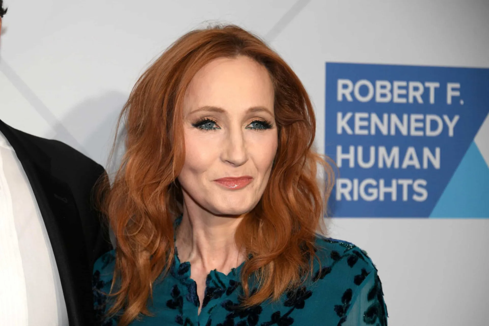 J. K. Rowling sorrindo em um evento, transmitindo sucesso e confiança.