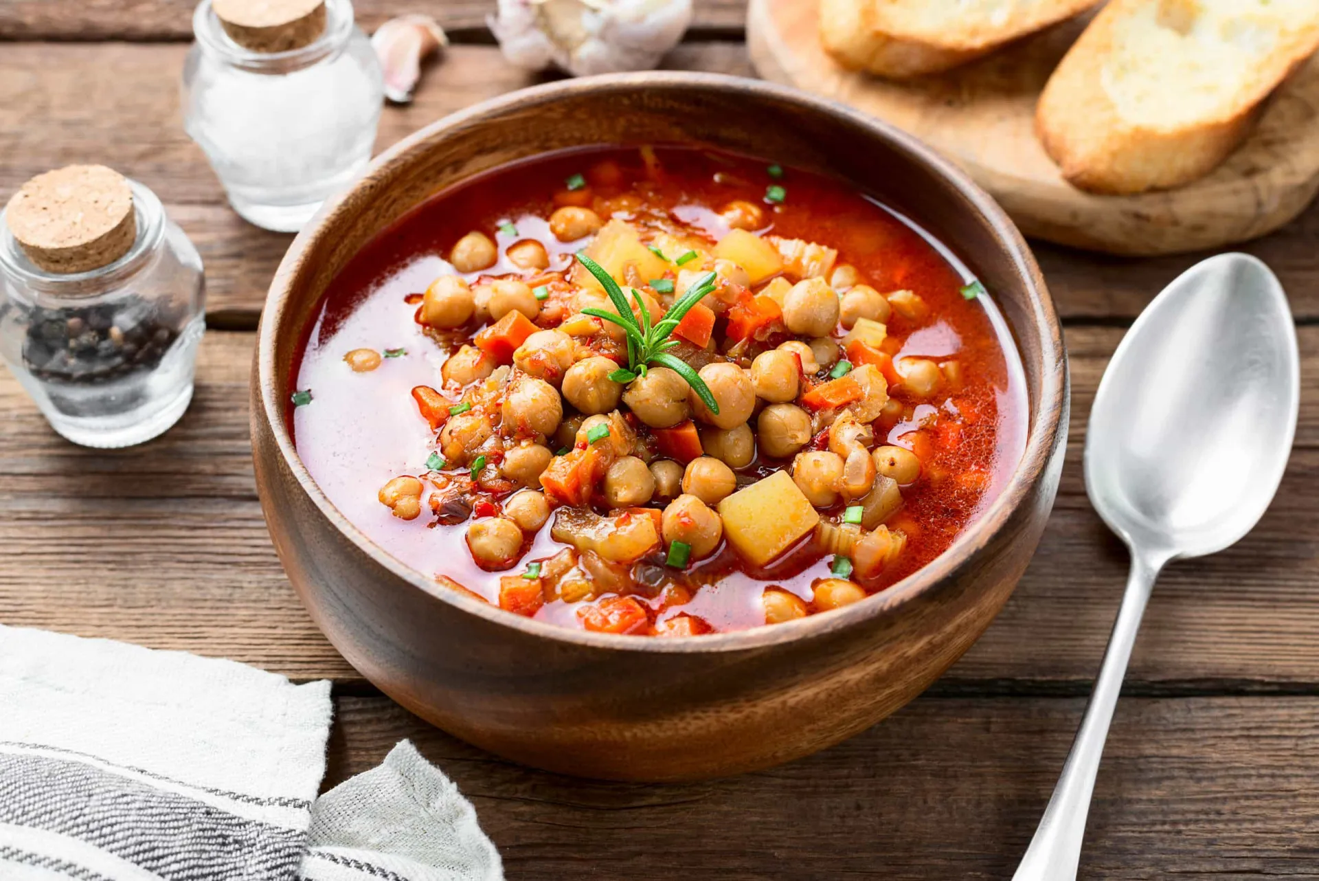 Uma tigela fumegante de sopa de grão-de-bico com legumes picados e ervas frescas.